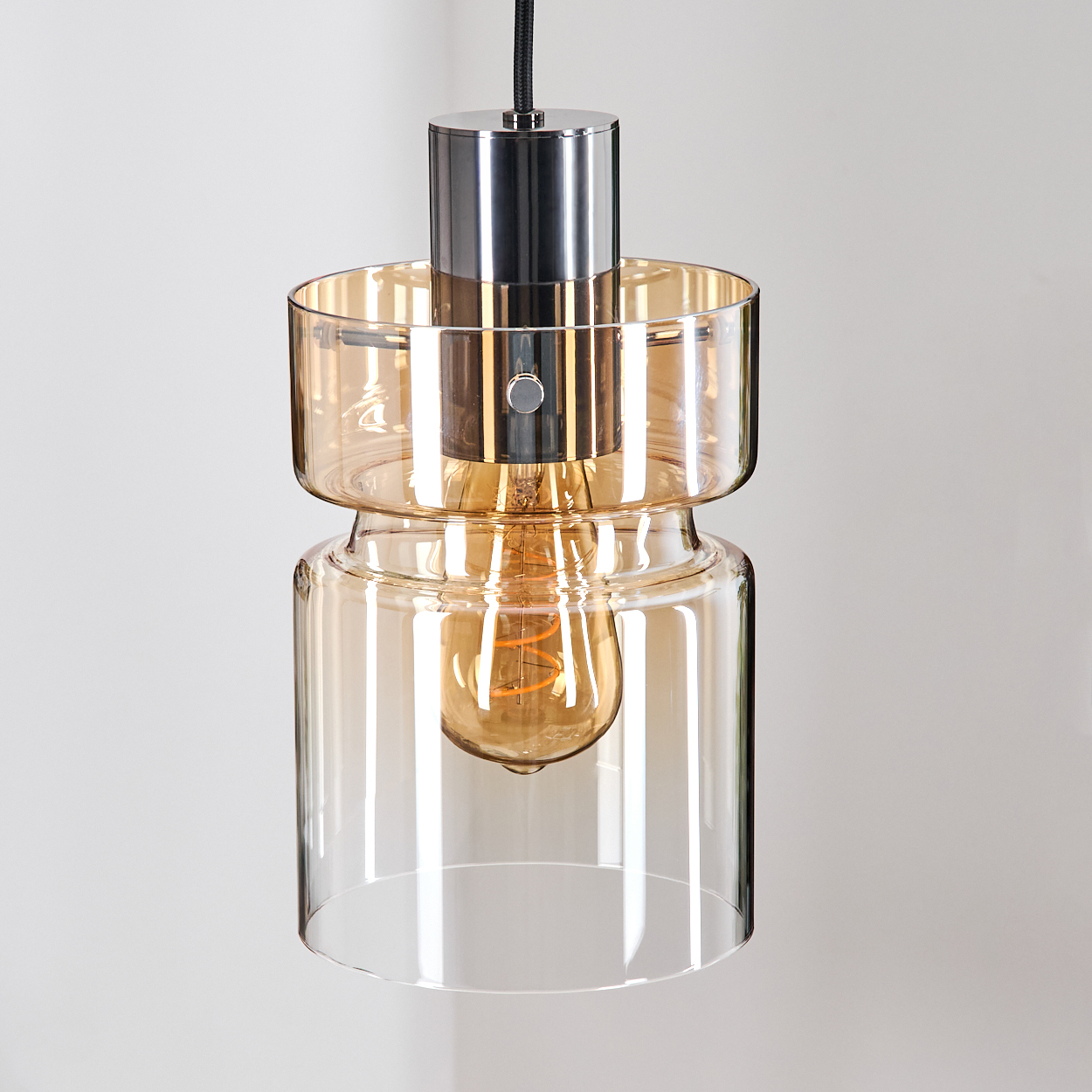Eine moderne Pendelleuchte mit zylindrischem Glasschirm und Metallaufsatz. Die Glühbirne ist innen sichtbar, mit warmer Farbe.