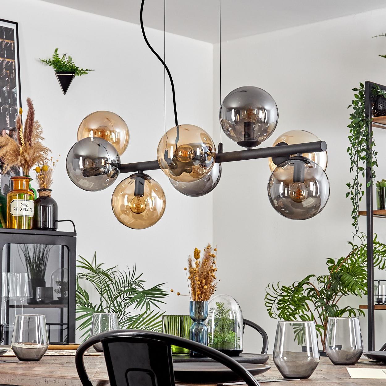 Ein modernes Esszimmer mit einem schwarzen Kronleuchter mit Glaskugeln. Pflanzen, Gläser und ein Tisch sind im Bild.