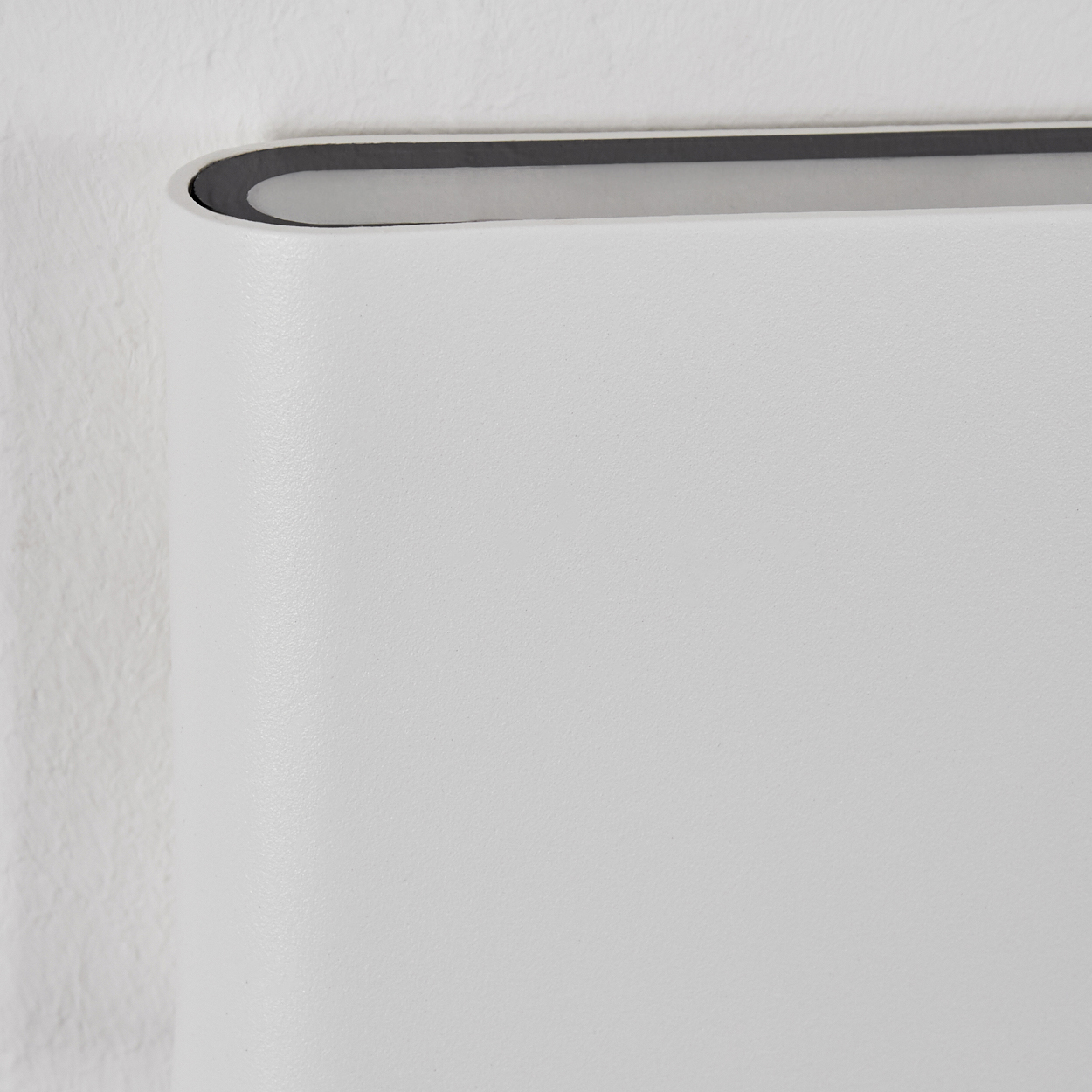 Nahaufnahme einer weißen Wand mit einem gebogenen Abschnitt. Oben ist eine vertiefte dunkle Linie zu sehen. Die Wand hat eine strukturierte Oberfläche.