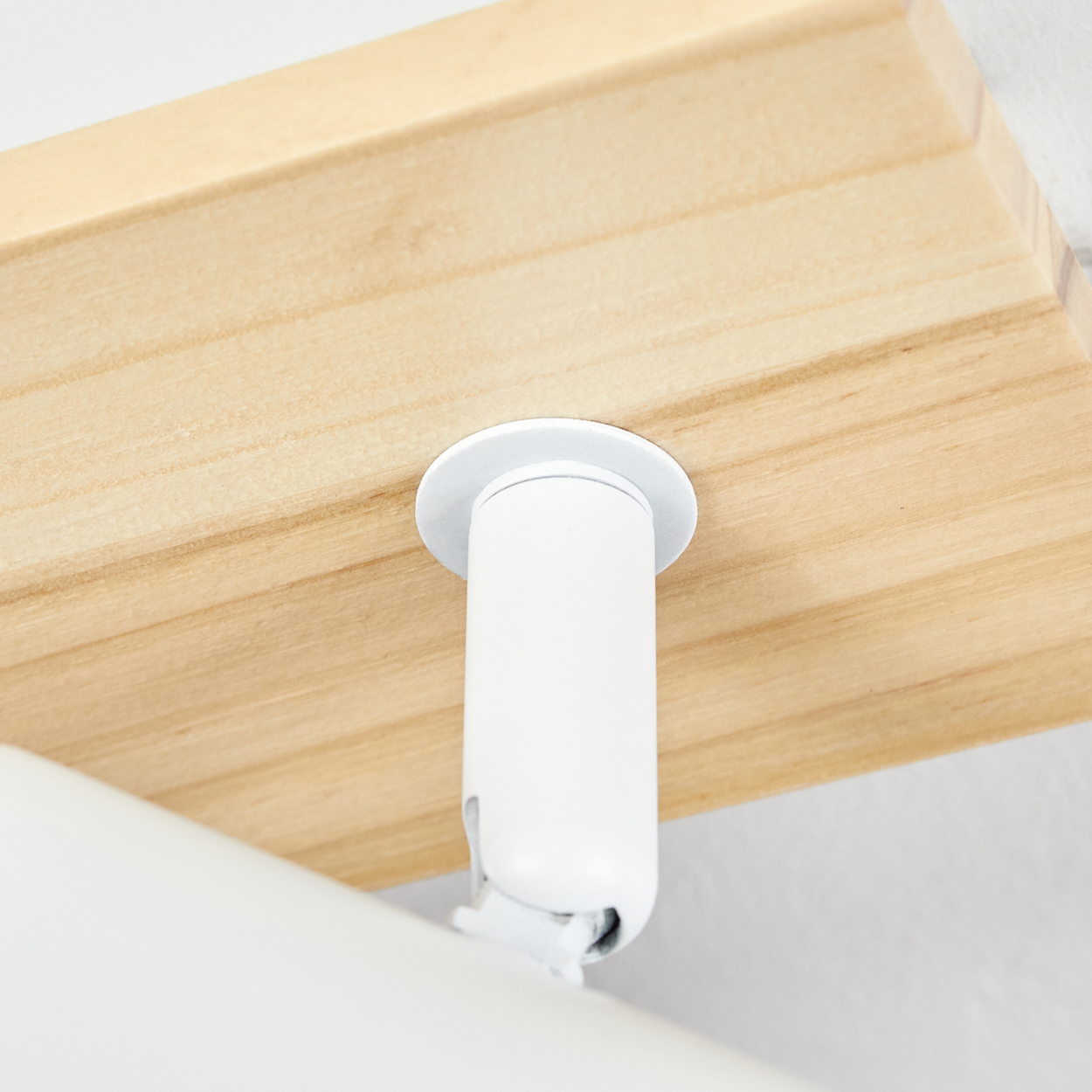 Eine weiße zylindrische Leuchte ist unter einem Holzregal montiert. Das Licht ist nach unten gerichtet. Der Hintergrund ist weiß.