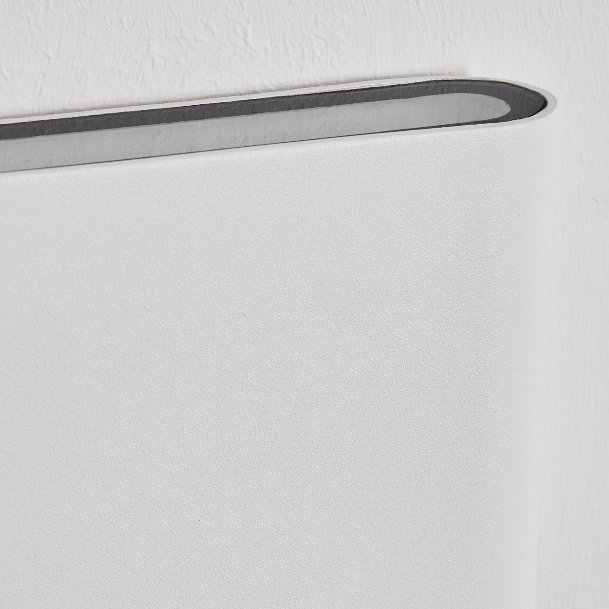 Nahaufnahme einer weißen Wand mit einem gebogenen, grau gefütterten Element oben. Die Wand hat eine strukturierte Oberfläche.