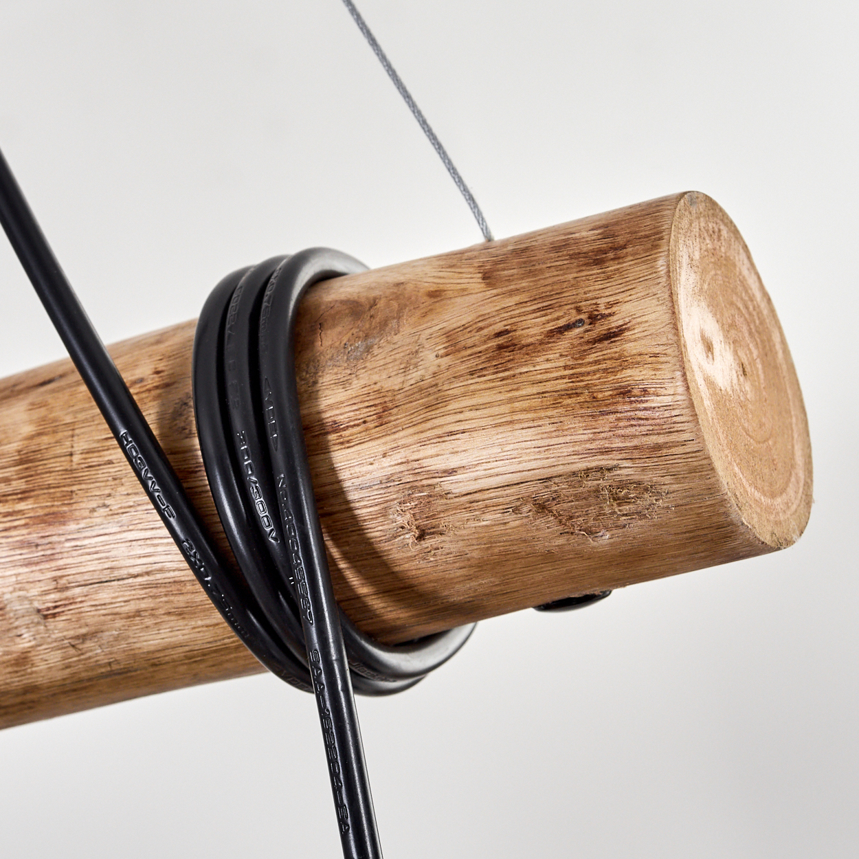 Ein Holzstamm mit schwarzen Kabeln, die darum gewickelt sind, an einem Draht vor weißem Hintergrund aufgehängt.