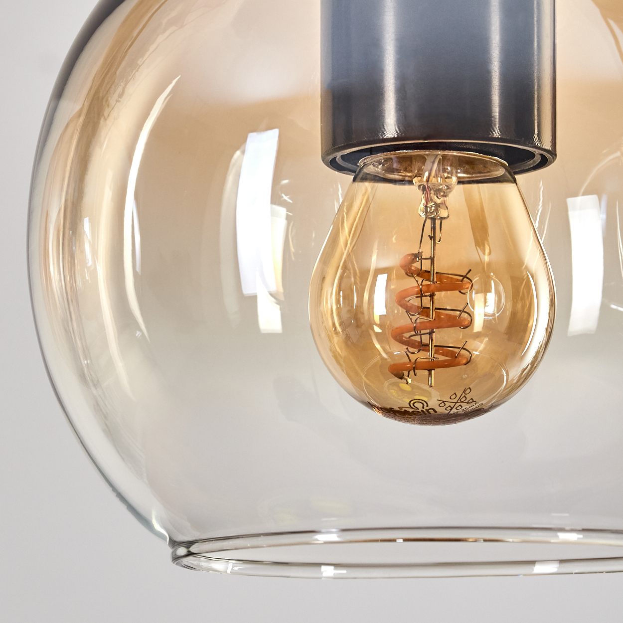Nahaufnahme einer Glühbirne in einer Glaskugel. Die Glühbirne hat einen spiralförmigen Glühdraht und das Glas hat eine warme, bernsteinfarbene Tönung.