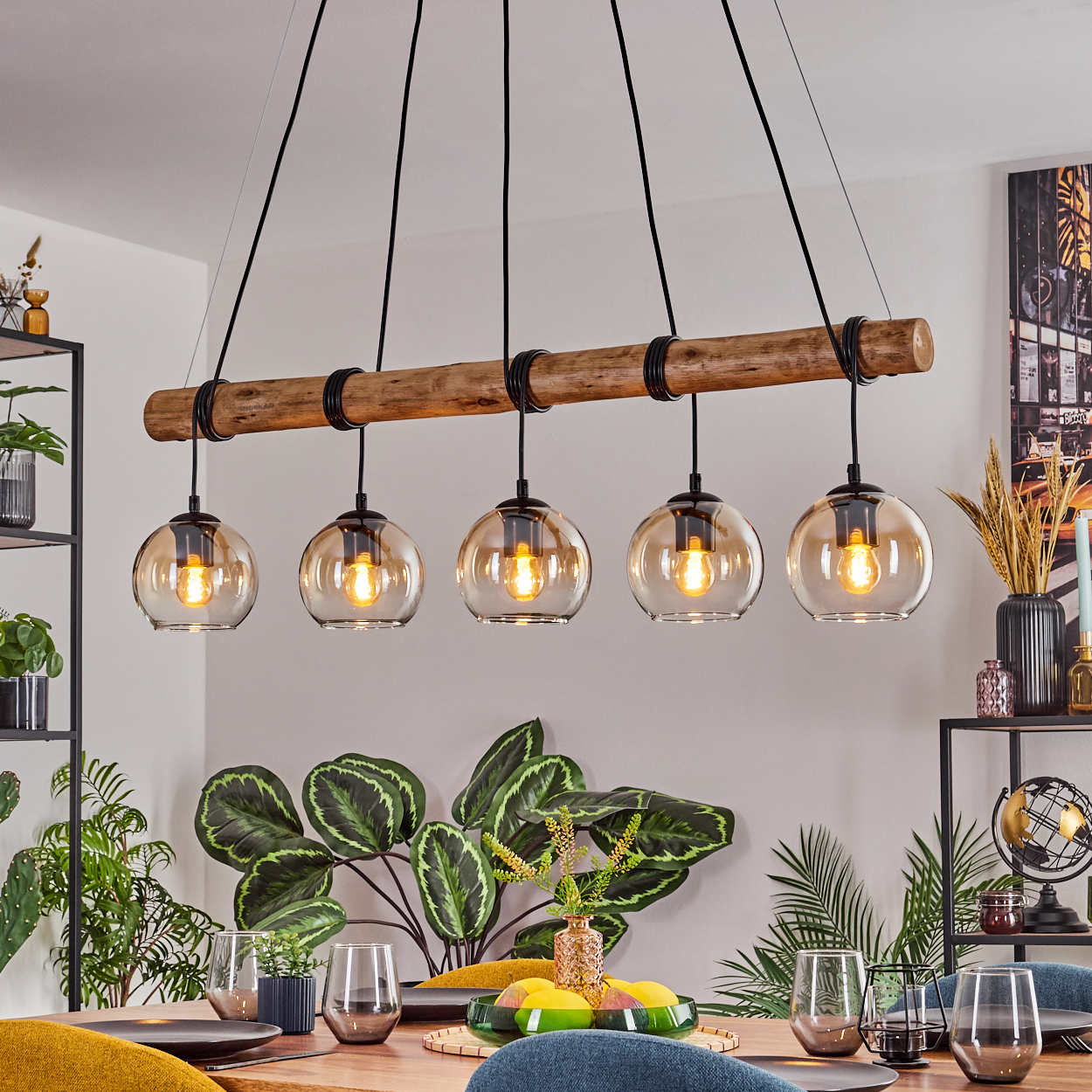 Esszimmer mit Holzbalken-Kronleuchter und fünf Glaskugelleuchten. Ein Tisch ist mit Gläsern und Pflanzen gedeckt.