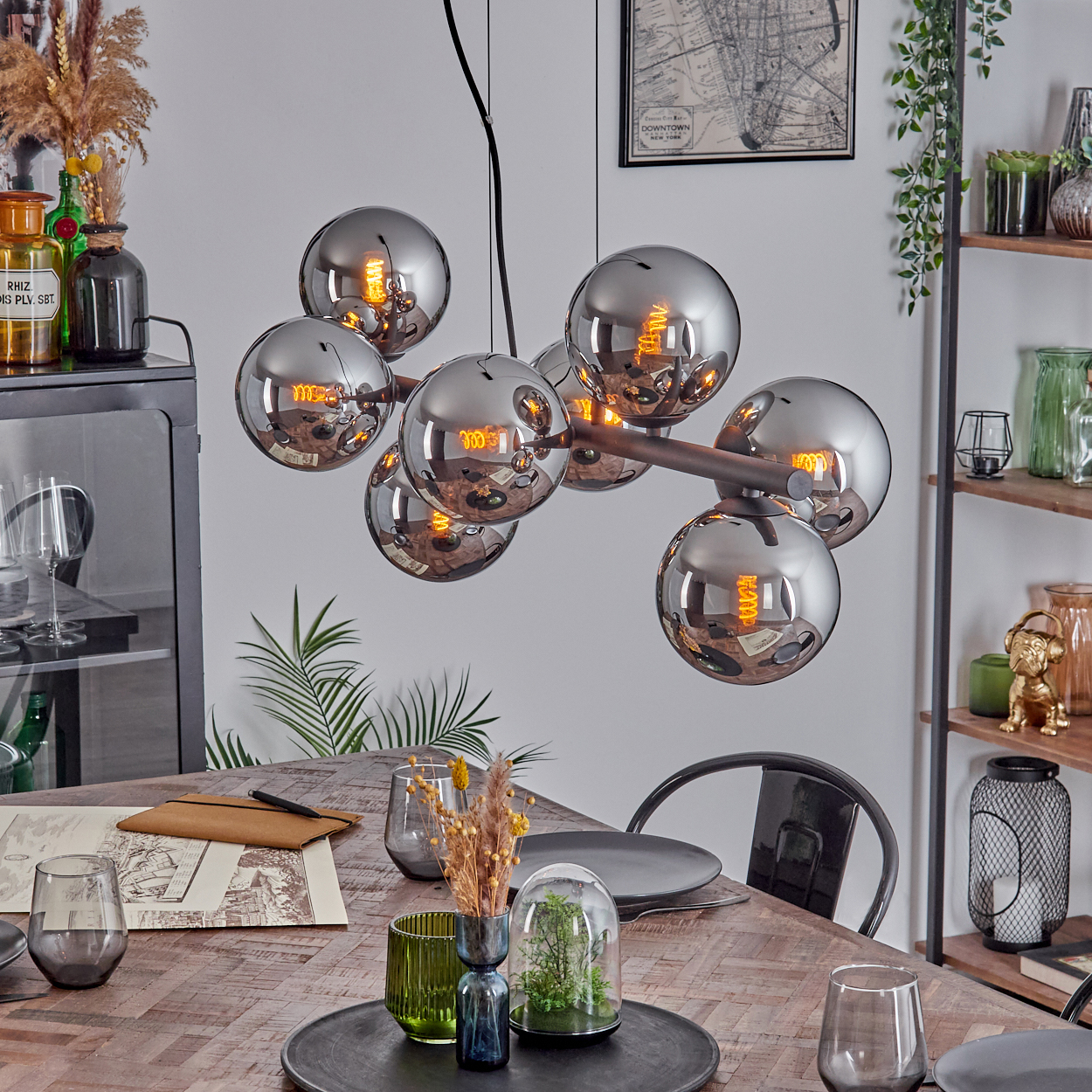 Ein Esszimmer mit Holztisch, moderner Kronleuchter mit kugelförmigen Lampen und Dekorationsgegenständen auf Regalen.