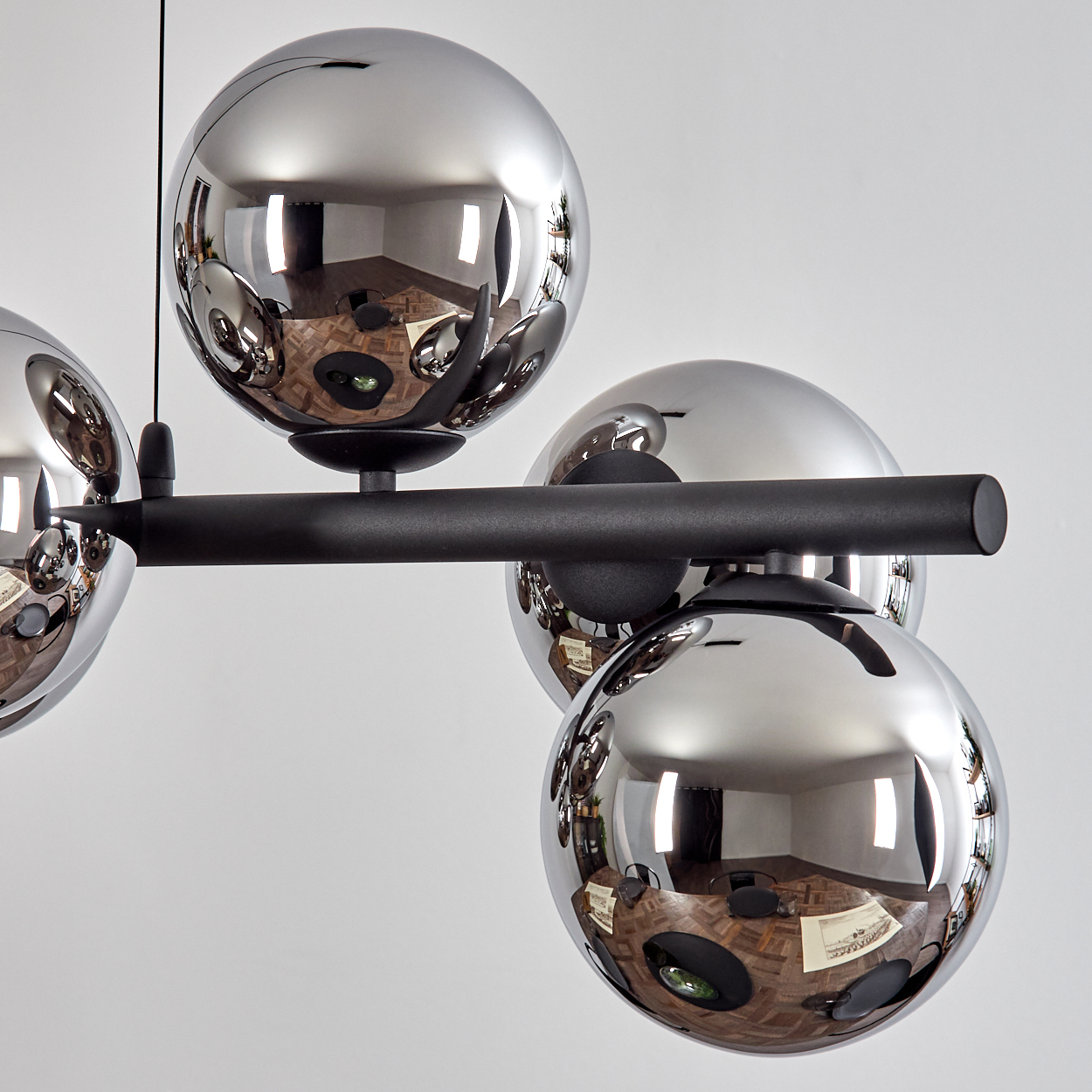Nahaufnahme einer modernen Chandelier mit kugelförmigen Chrombirnen, die einen Raum reflektieren. Schwarze Halterung auf weißem Hintergrund.