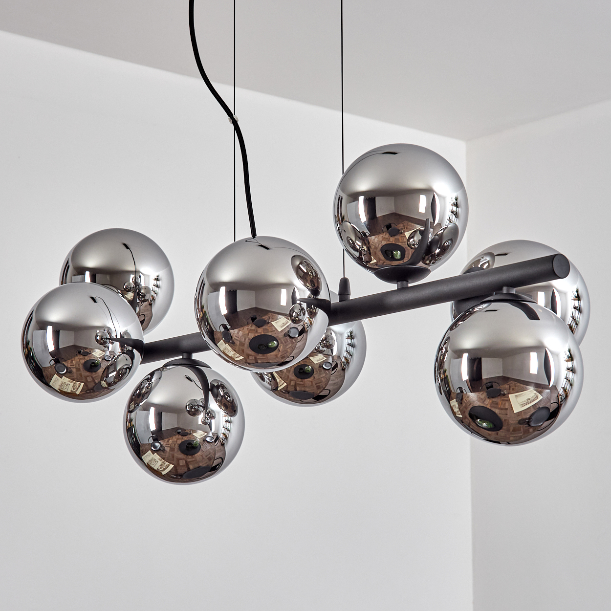 Eine moderne Pendelleuchte mit verchromten Kugeln, die den Raum reflektieren. Die Kugeln sind an einem schwarzen Balken befestigt.