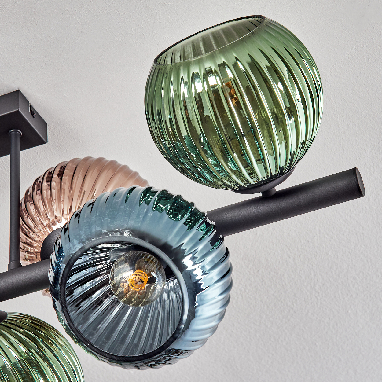 Eine moderne Deckenleuchte mit vier bunten Glaskugeln. Die Schirme sind grün, blau und pfirsichfarben, montiert auf einer schwarzen Metallstange.