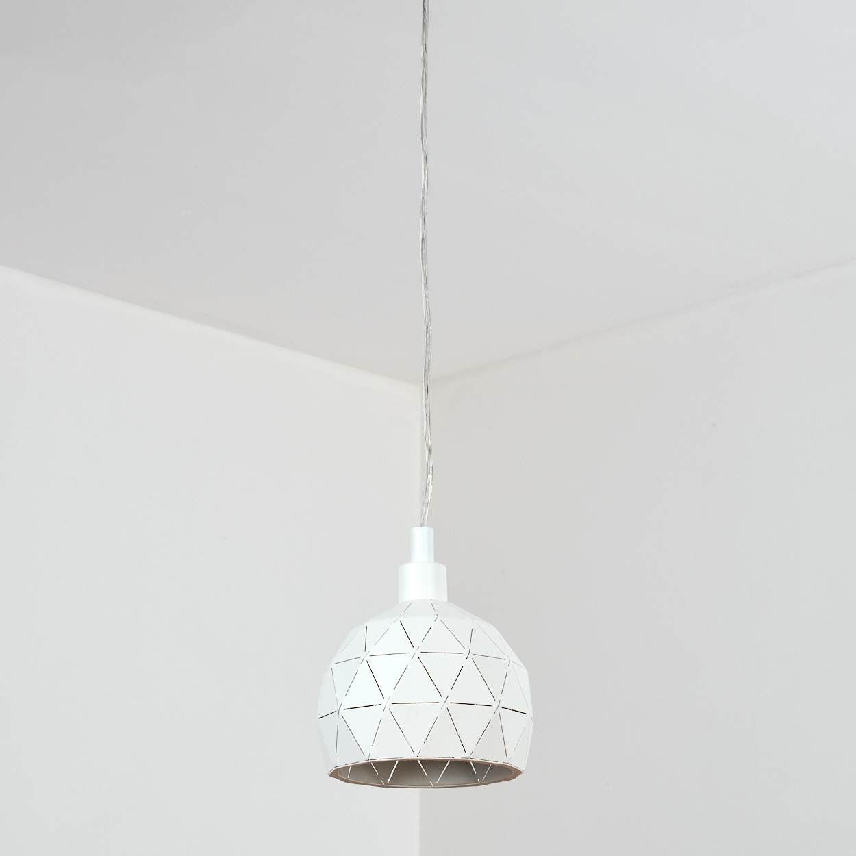 Eine weiße geometrische Pendelleuchte hängt von der Decke. Der Hintergrund ist eine weiße Wand- und Deckenecke.