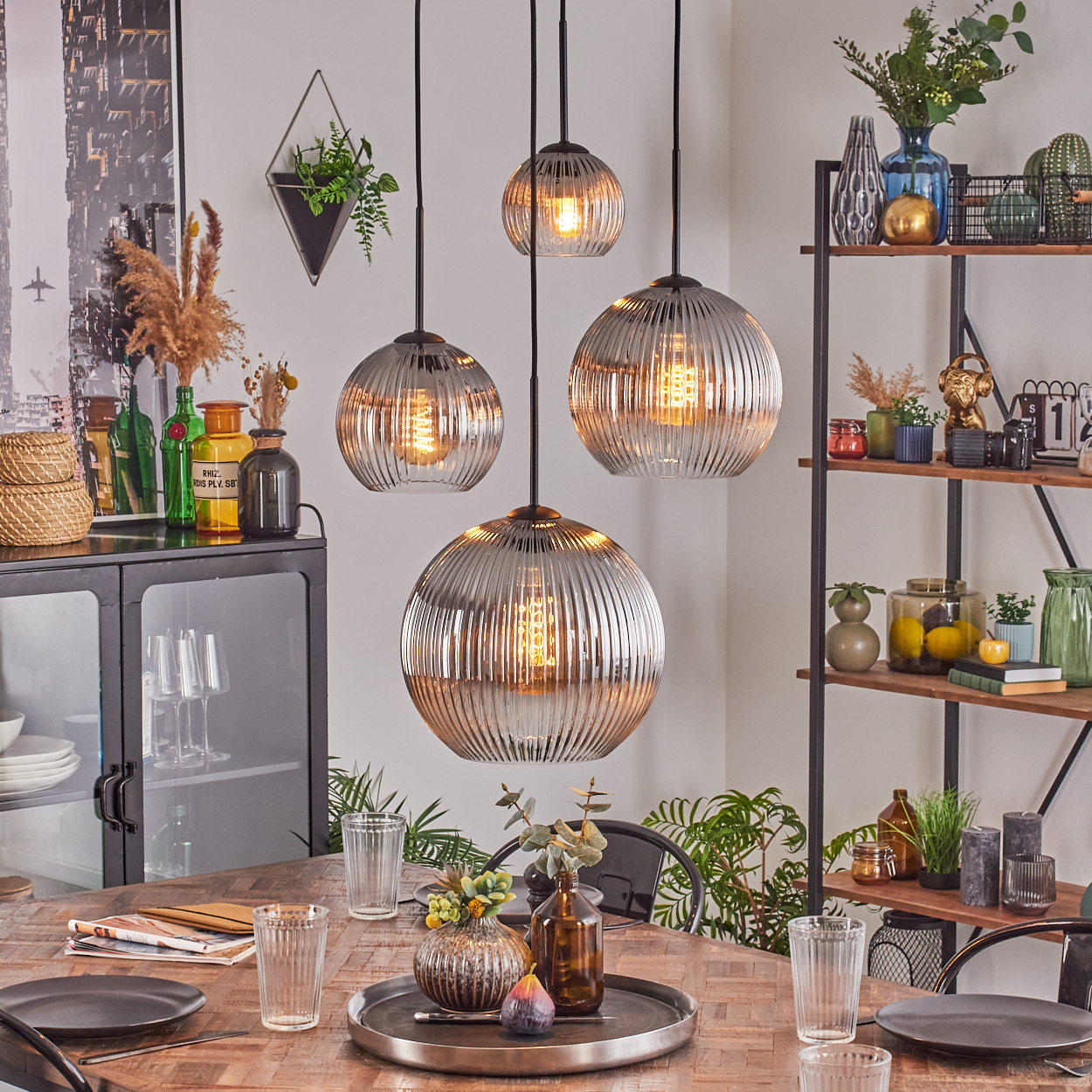 Esszimmer mit Holztisch, Hängelampen, Gläsern, Vase mit Blumen und einem Regal mit Dekorationen.