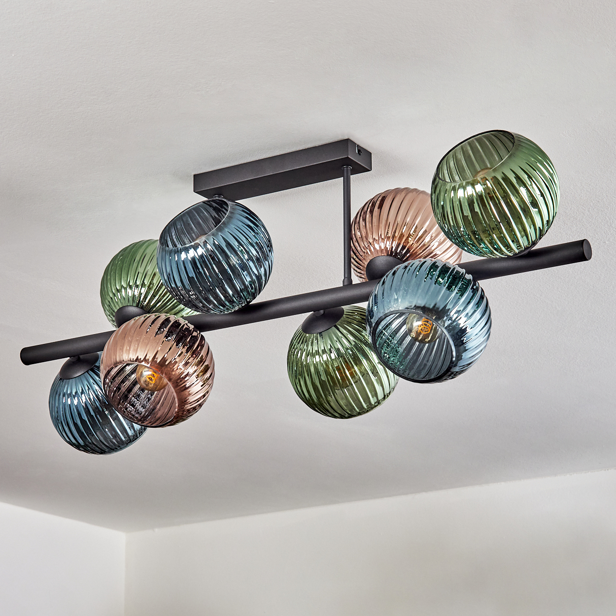 Eine moderne Deckenleuchte mit neun kugelförmigen, gerippten Glasschirmen in verschiedenen Farben hängt an einem schwarzen Rahmen.