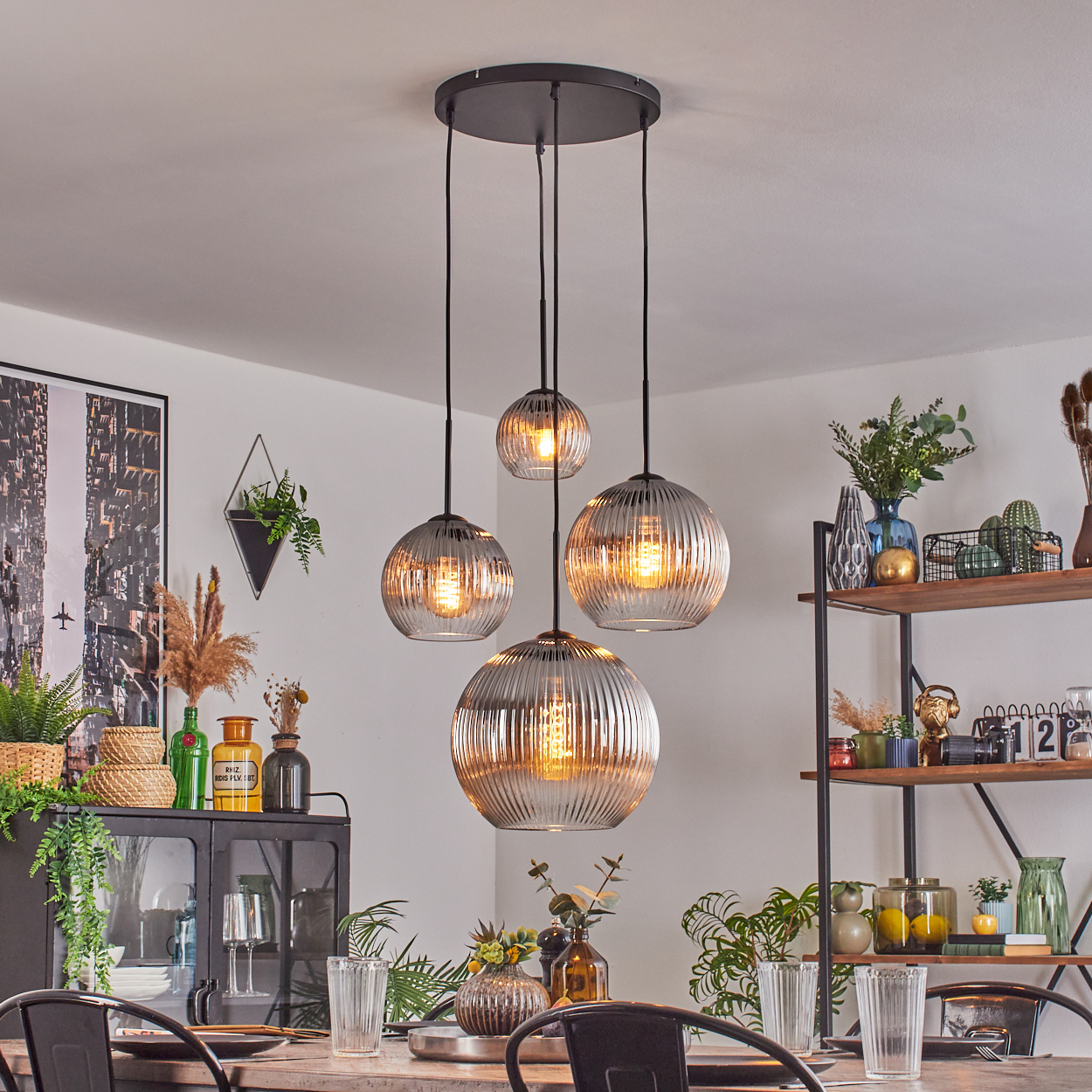 Esszimmer mit Hänge-Globus-Leuchten, Tisch mit Gläsern, schwarzen Metallstühlen und Regalen mit Dekoration.