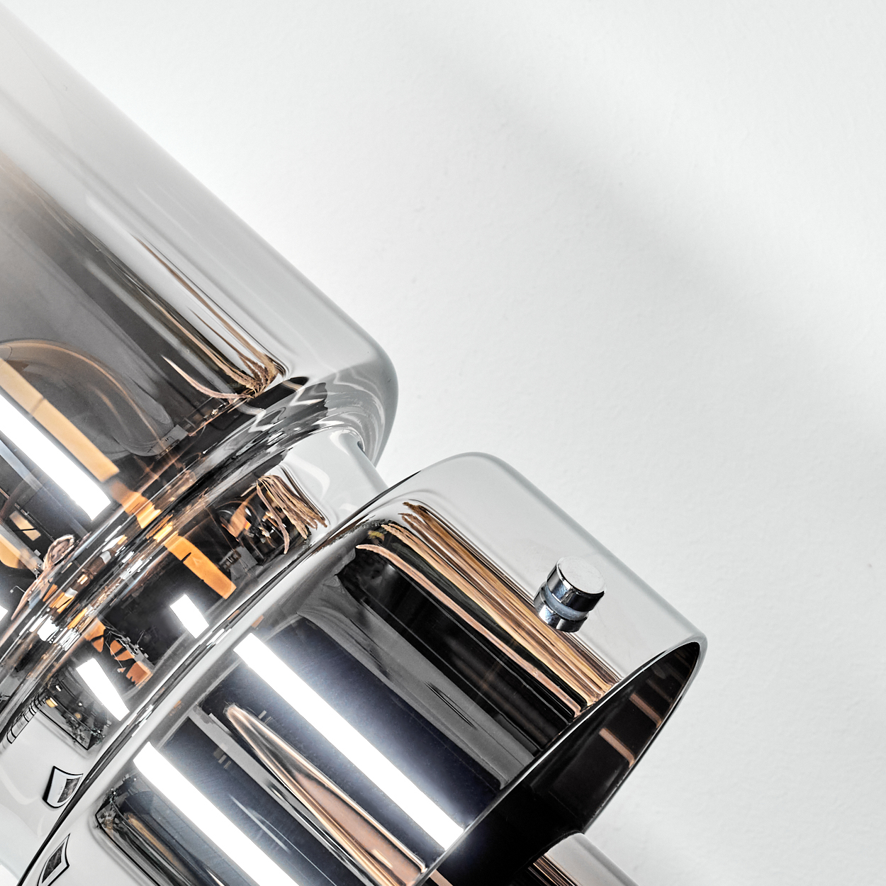 Nahaufnahme eines glänzenden Metallobjekts mit einem Glasrohr. Das Objekt hat eine reflektierende Oberfläche, der Hintergrund ist weiß.