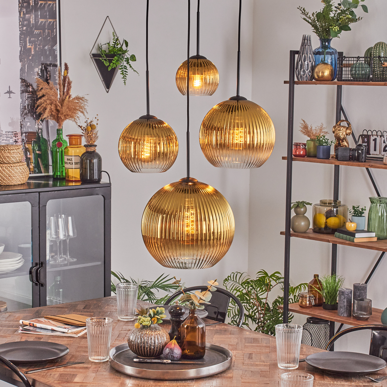 Esszimmer mit Holztisch, goldenen Pendelleuchten, Glasvasen, Pflanzen und einem schwarzen Metallregal mit Dekorationen.