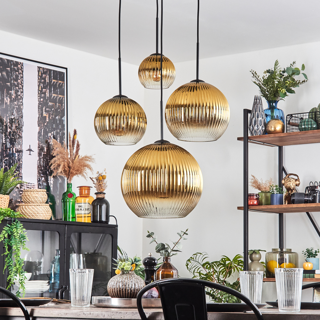 Esszimmer mit goldenen Hängelampen, Tisch mit Gläsern und Pflanzen, schwarzem Schrank und Regal.