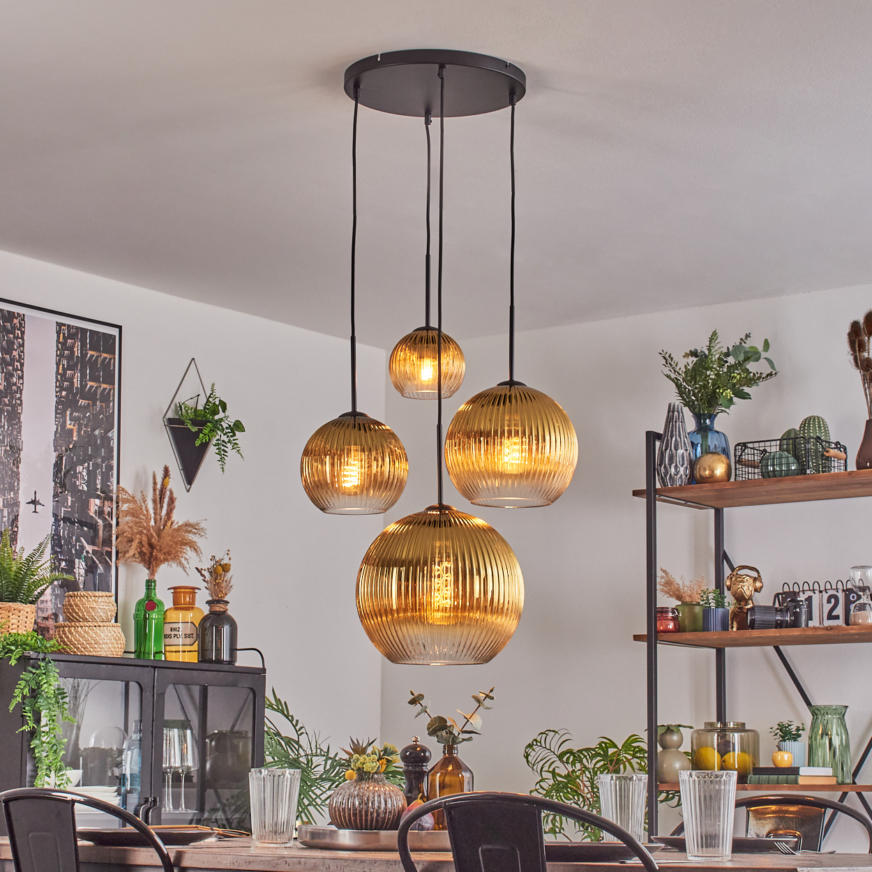 Esszimmer mit hängenden goldenen Lampen. Ein Tisch ist mit Gläsern gedeckt. Regale mit Dekorationen sind im Hintergrund.