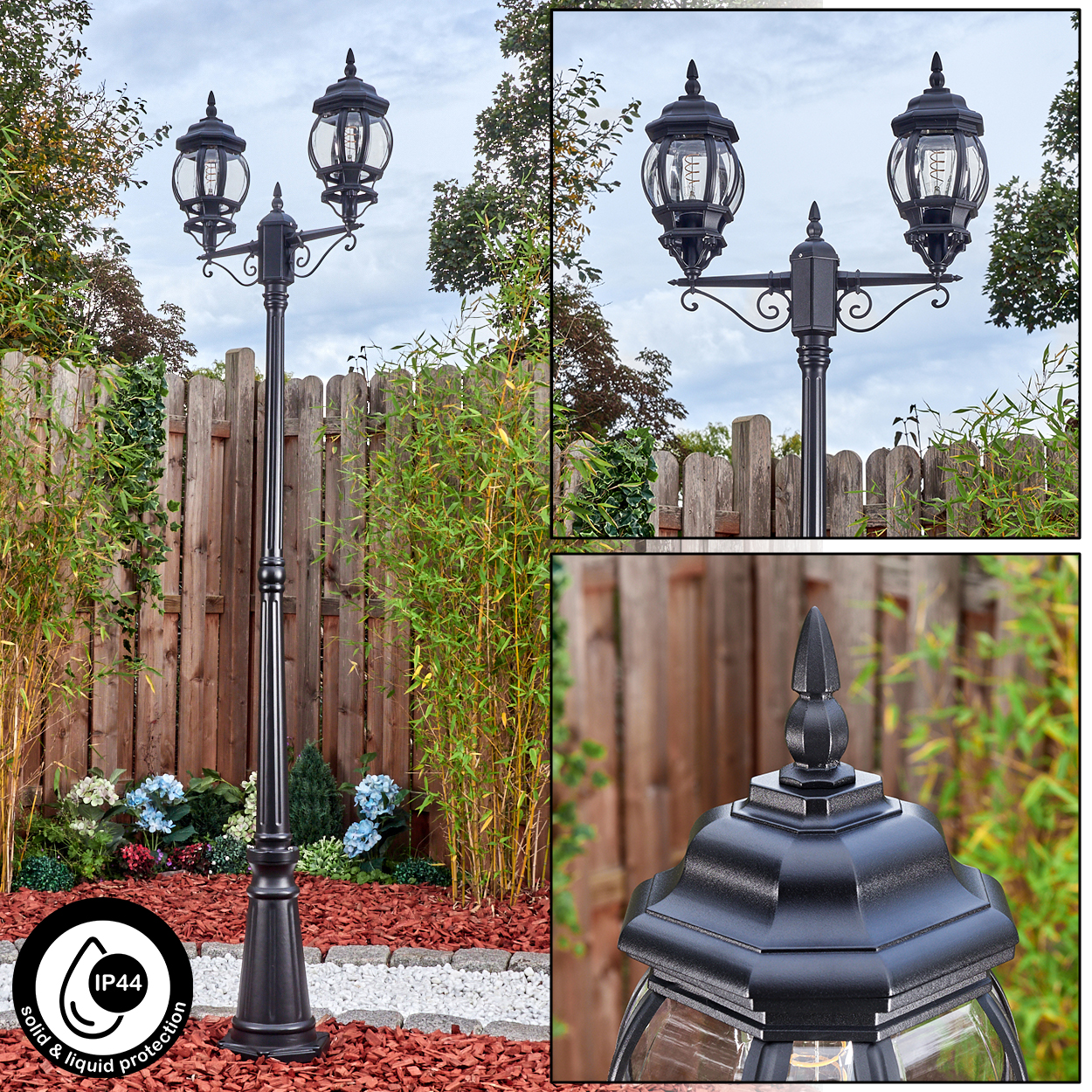 Eine schwarze Außenlaterne mit zwei Lampen. Sie steht vor einem Holzzaun, umgeben von Pflanzen und einem bewölkten Himmel.