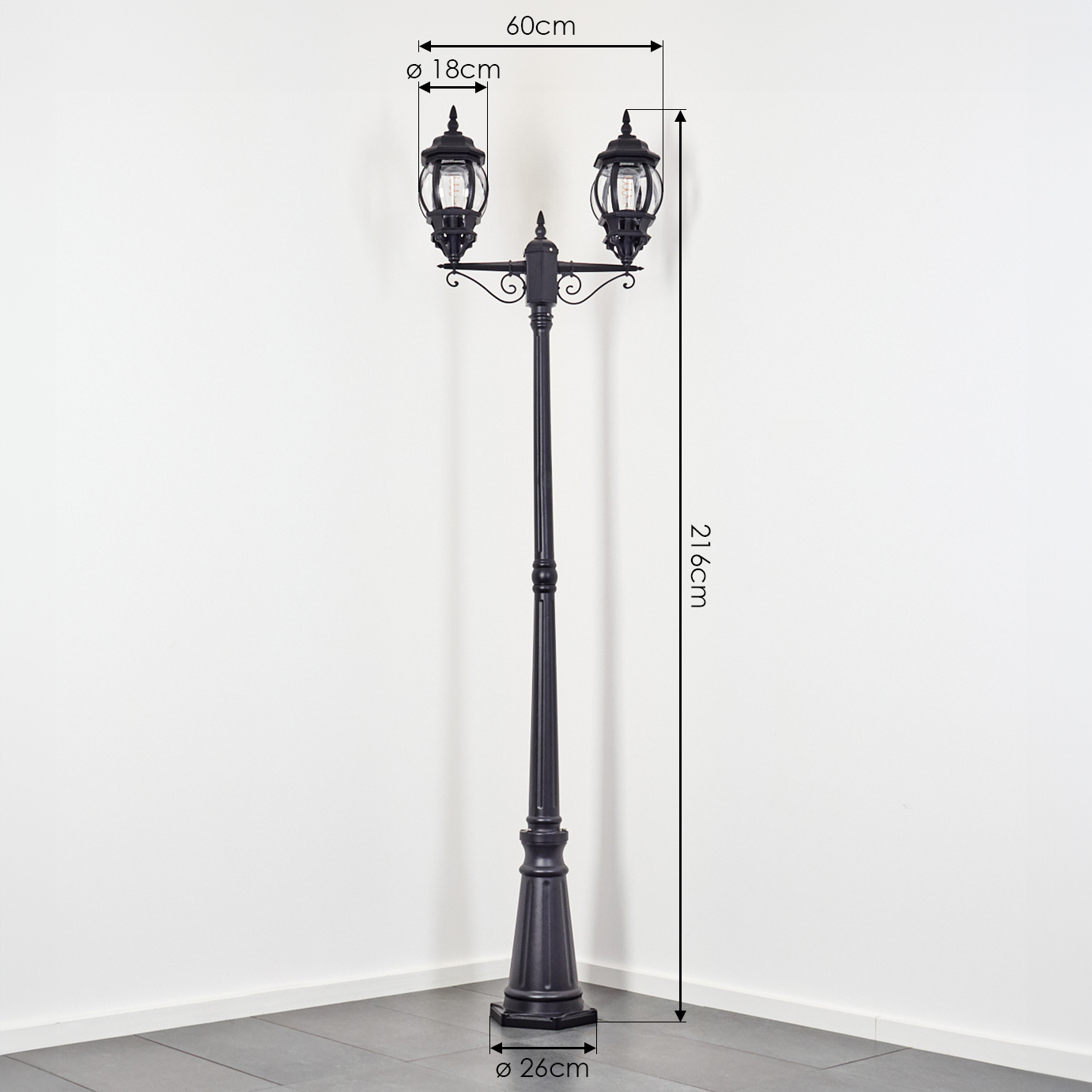 Eine schwarze Straßenlaterne mit zwei Lichtern, Maße sind beschriftet. Sie steht vor einer weißen Wand und grauem Boden.