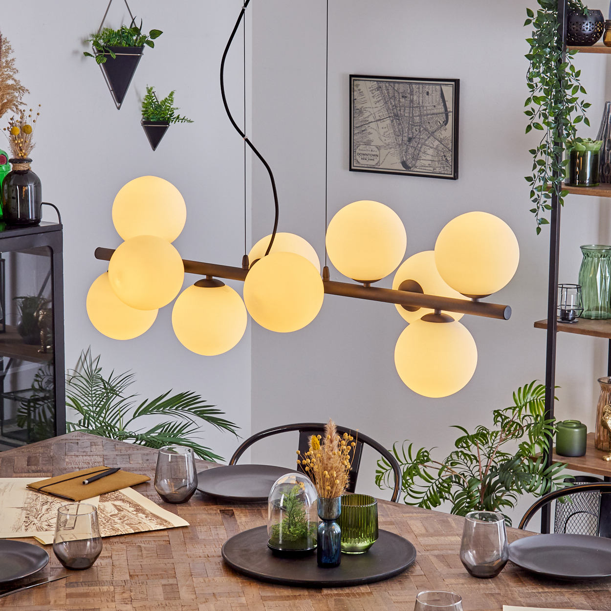 Esszimmer mit Holztisch. Eine Hängelampe mit Kugelleuchten hängt darüber. Pflanzen und Dekoration sind im Raum vorhanden.