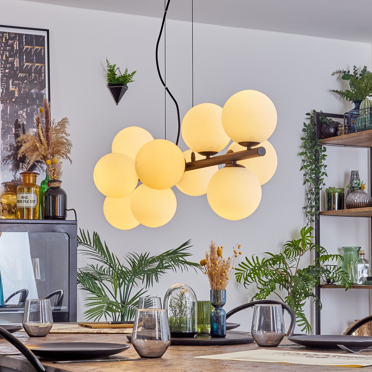 Esszimmer mit Holztisch, Gläsern, schwarzen Tellern und Kronleuchter mit kugelförmigen Lichtern. Pflanzen und Dekorationen vorhanden.