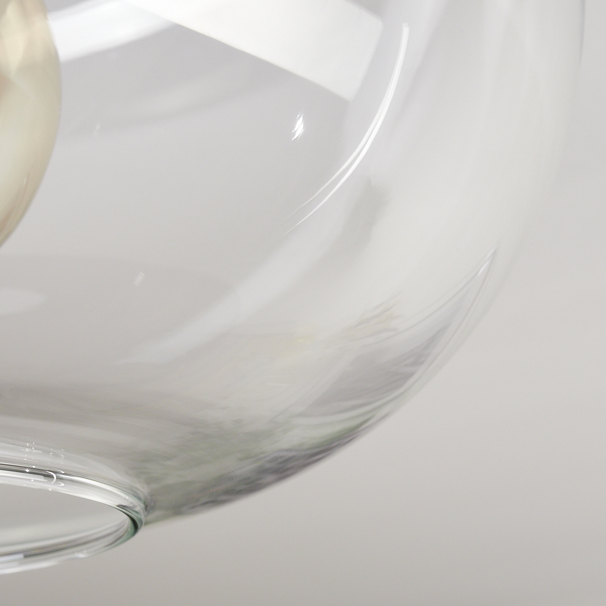 Nahaufnahme eines transparenten Glasobjekts. Das Glas ist gebogen und reflektiert das Licht. Der Hintergrund ist ein sanftes Weiß.
