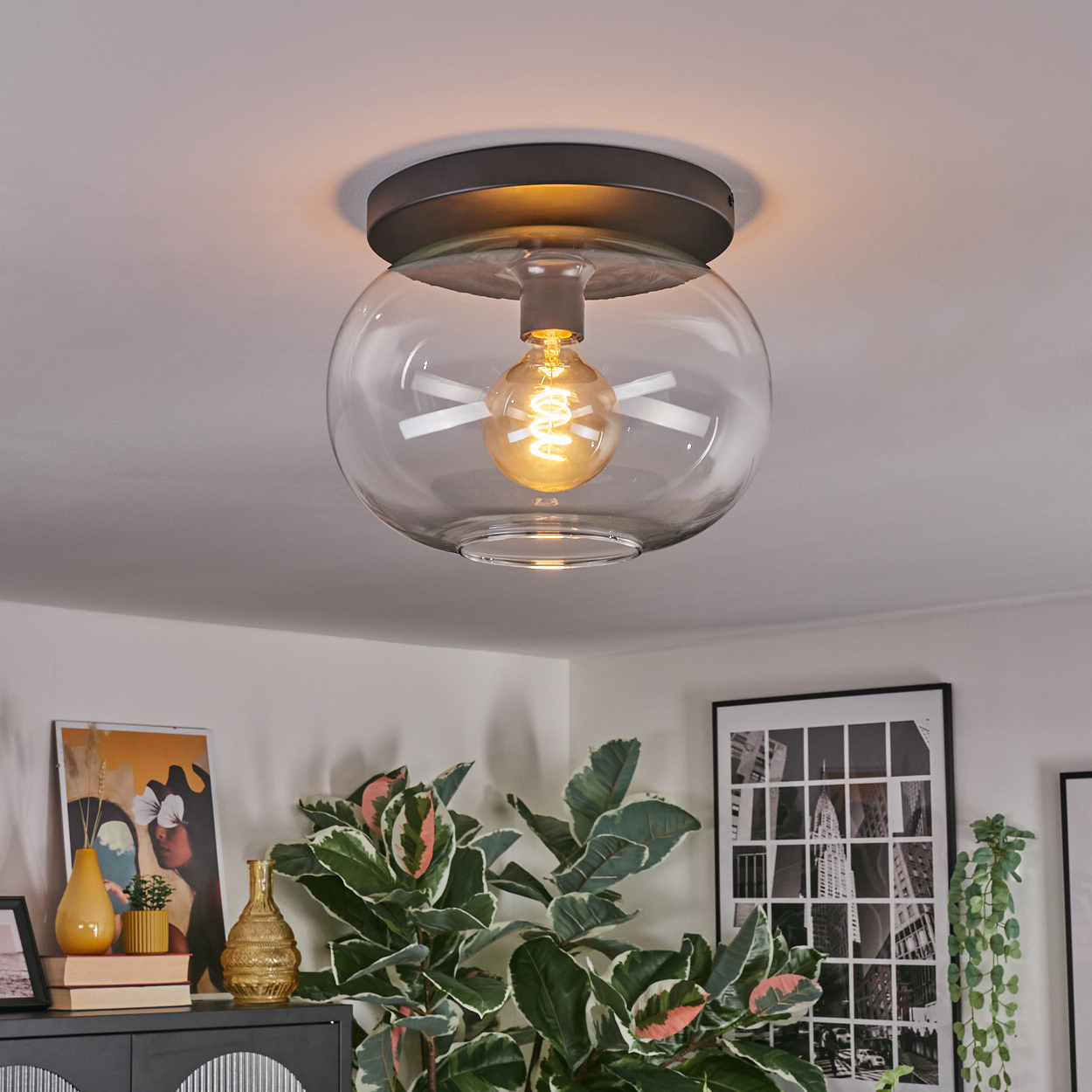 Eine moderne Deckenleuchte mit einem Glasschirm, die einen Raum mit Kunstwerken und Pflanzen beleuchtet.