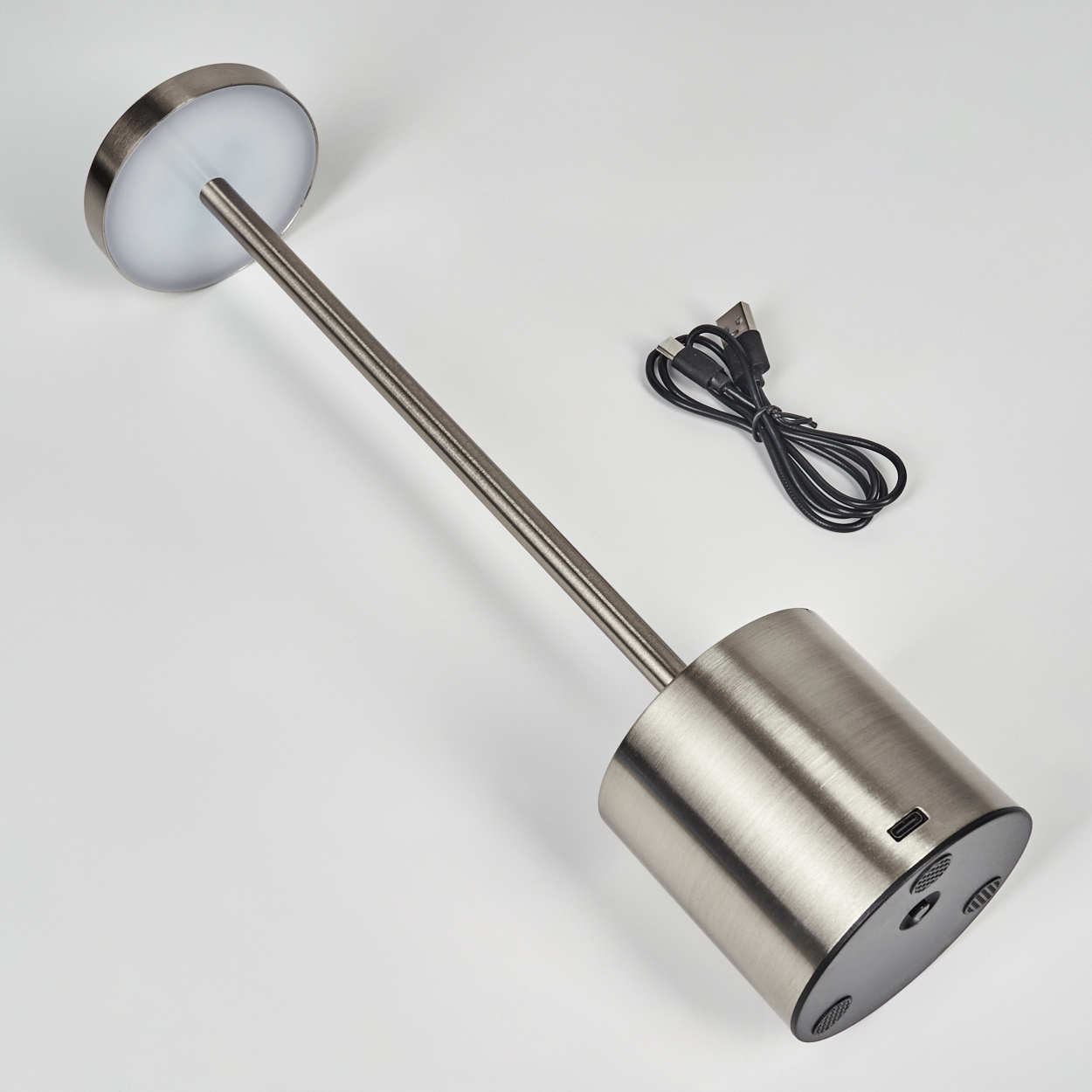 Eine moderne silberne Lampe mit rundem Kopf und zylindrischem Fuß, zusammen mit einem schwarzen USB-Kabel, alles auf weißem Grund.