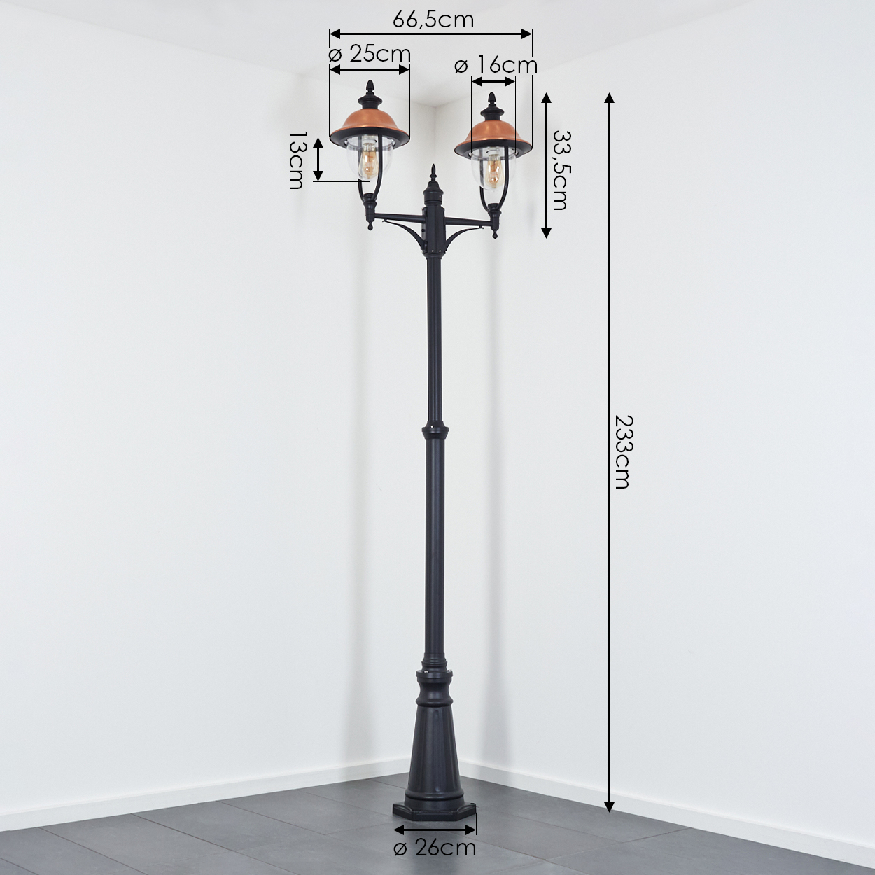 Eine schwarze Straßenlaterne mit zwei Lichtern, kupferfarbenen Schirmen und Abmessungen in Zentimetern, vor weißer Wand und grauem Boden.