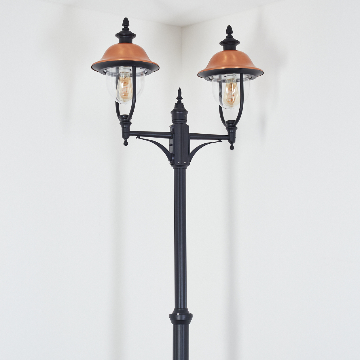 Eine schwarze und kupferfarbene Außenlampe mit zwei Lichtern, vor einer weißen Wand.