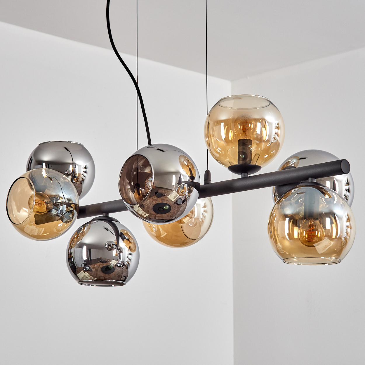 Eine moderne Deckenlampe mit mehreren kugelförmigen Lichtern. Einige sind verspiegelt, andere bernsteinfarben. Die Leuchte hängt von der weißen Decke.