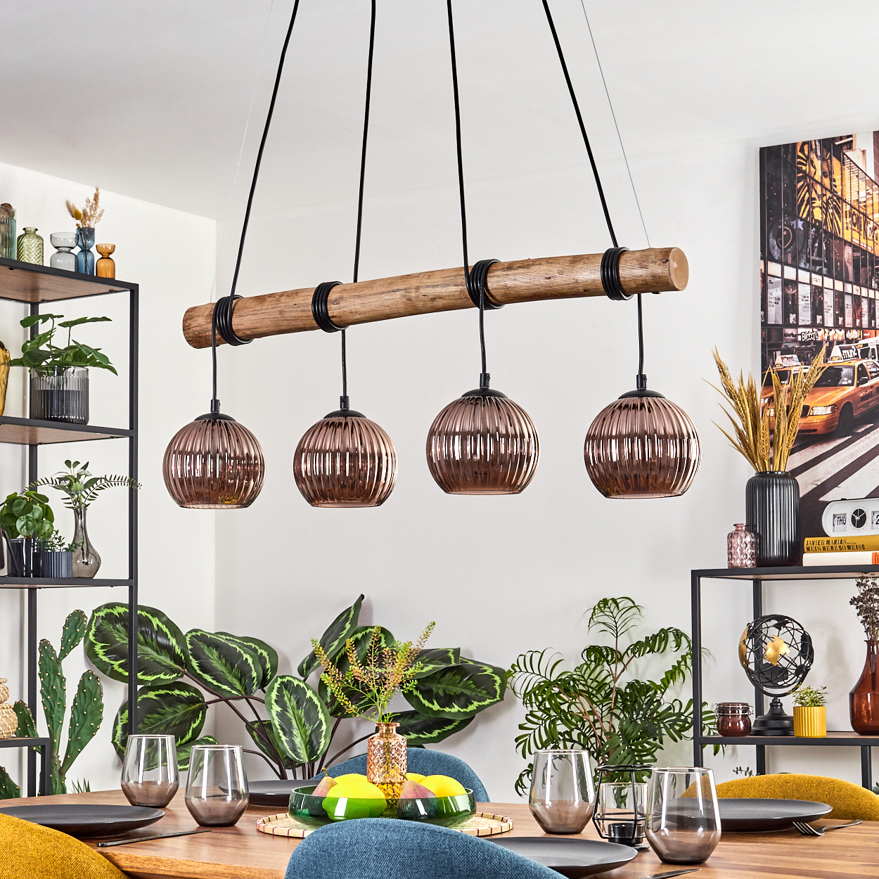Ein Esszimmer mit Holztisch, vier kupferfarbenen Pendelleuchten, Pflanzen und Gläsern. Ein New York City Bild hängt an der Wand.