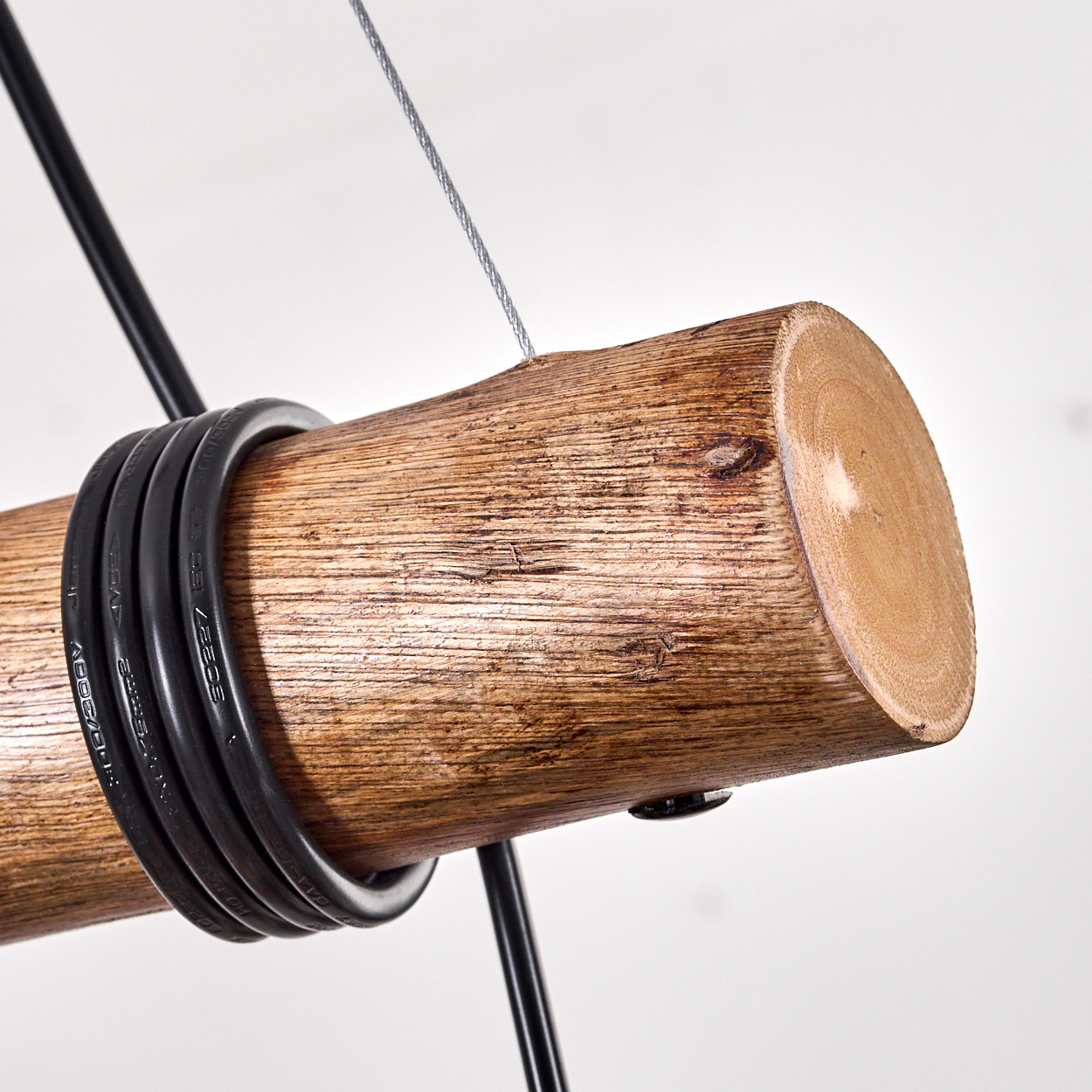 Nahaufnahme eines Holzstamms mit einem schwarzen Kabel darum. Ein Metalldraht und ein schwarzes Metallgestell sind ebenfalls sichtbar.