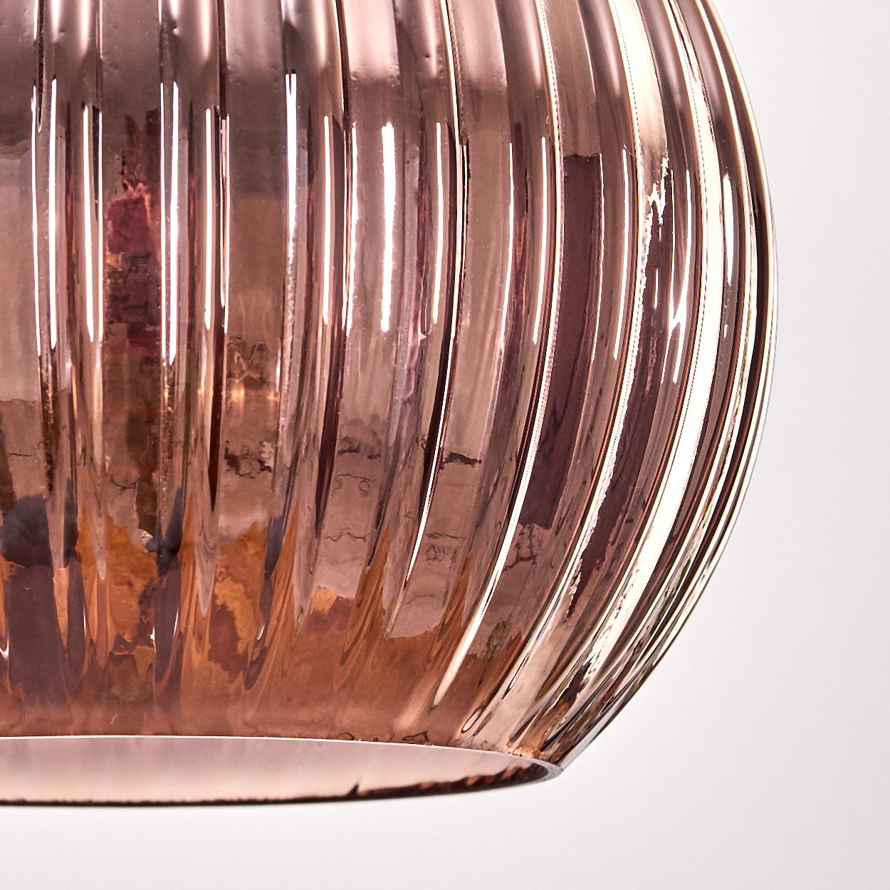 Nahaufnahme eines kupferfarbenen, gerippten Glasobjekts vor weißem Hintergrund. Das Glas reflektiert Licht.