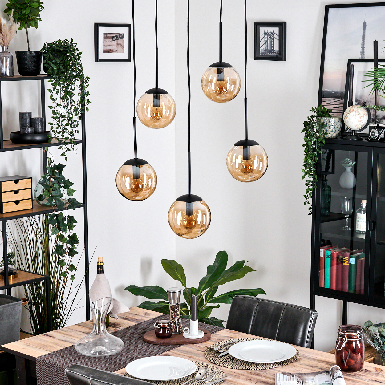 Esszimmer mit Holztisch, Hängelampen, Pflanzen und einem schwarzen Schrank. Tisch mit Tellern und Gläsern gedeckt.