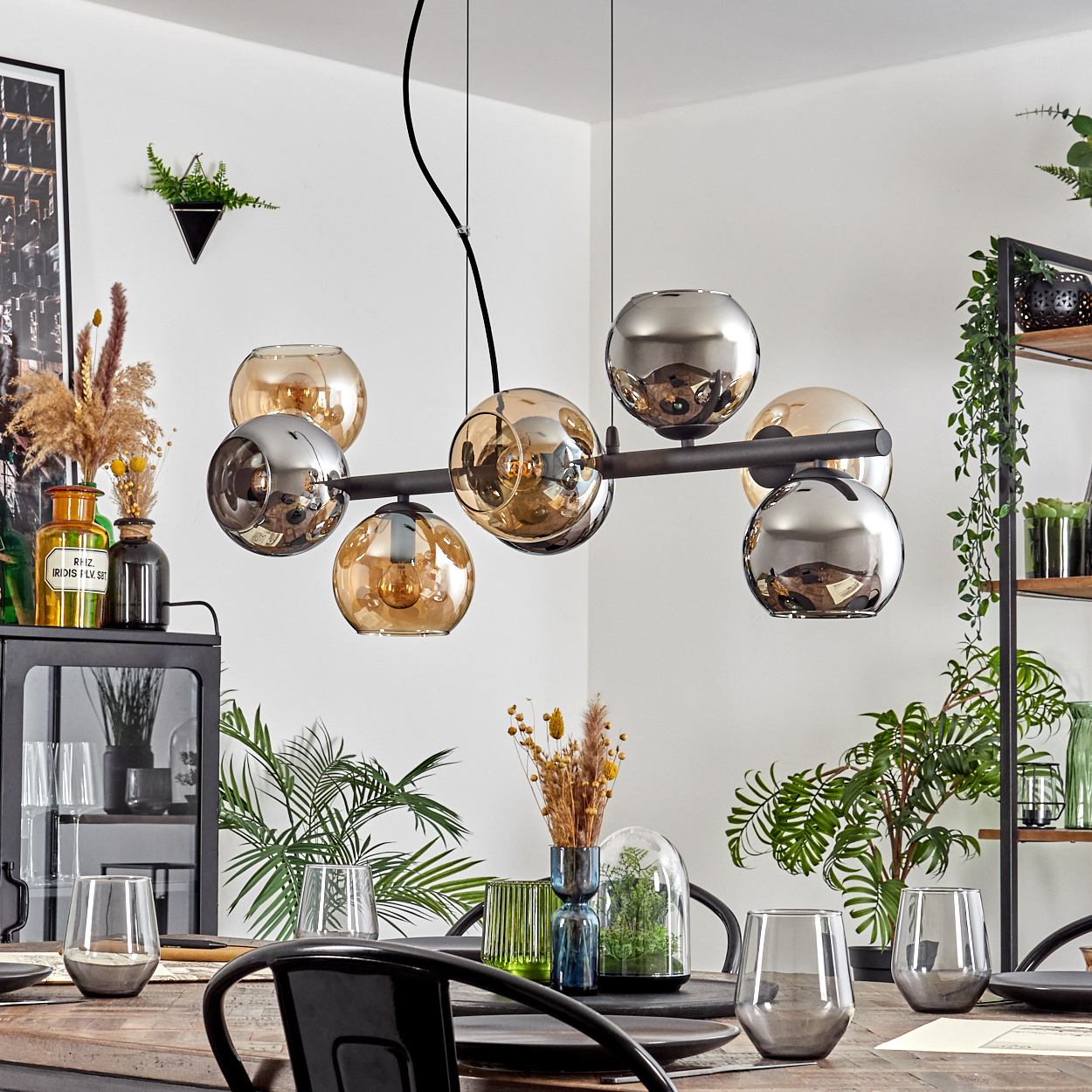 Esszimmer mit Holztisch, modernem Kronleuchter mit Glaskugeln und Zierpflanzen. Die Umgebung ist hell und einladend.
