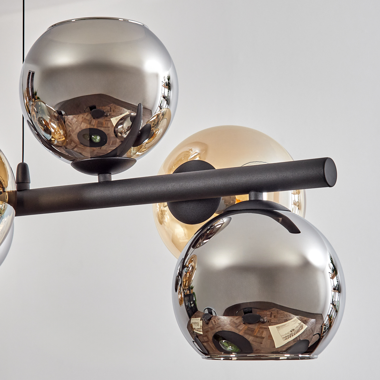 Eine moderne Deckenleuchte mit mehreren kugelförmigen Glasschirmen in Silber und Bernstein, die den Raum widerspiegeln. Schwarzer Metallrahmen.
