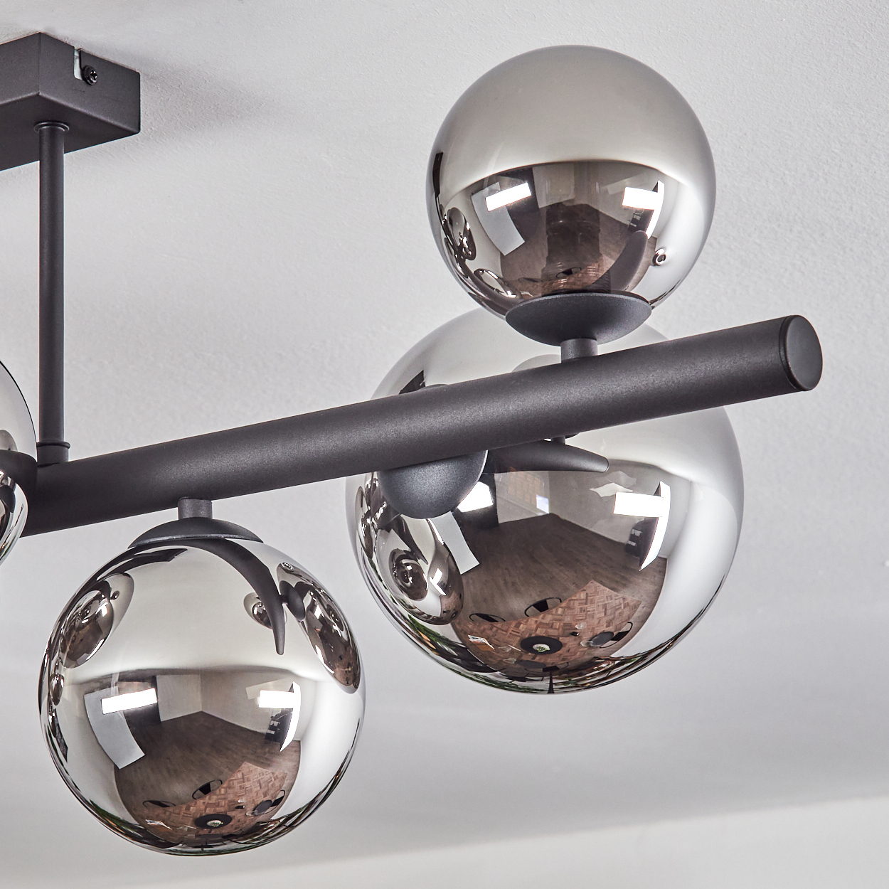 Eine moderne Deckenleuchte mit vier reflektierenden, kugelförmigen Schirmen. Die Leuchte ist schwarz, mit weißer Decke im Hintergrund. Die Kugeln spiegeln den Raum.