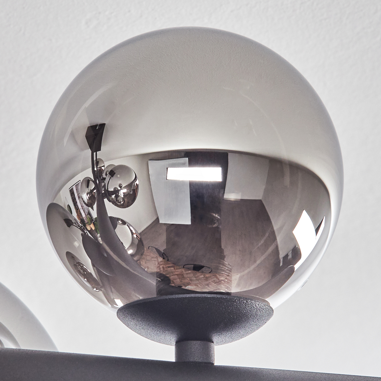 Nahaufnahme einer Glaskugel-Leuchte. Die Kugel reflektiert einen Raum mit Objekten und Leuchten. Der Sockel ist dunkelgrau.