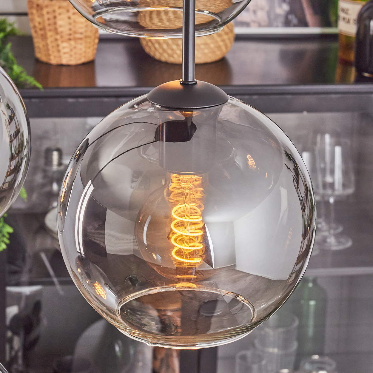 Nahaufnahme einer Glaskugel-Hängelampe mit einer warmen, spiralförmigen Glühbirne. Im Hintergrund ein Regal und andere Dekorationsgegenstände.