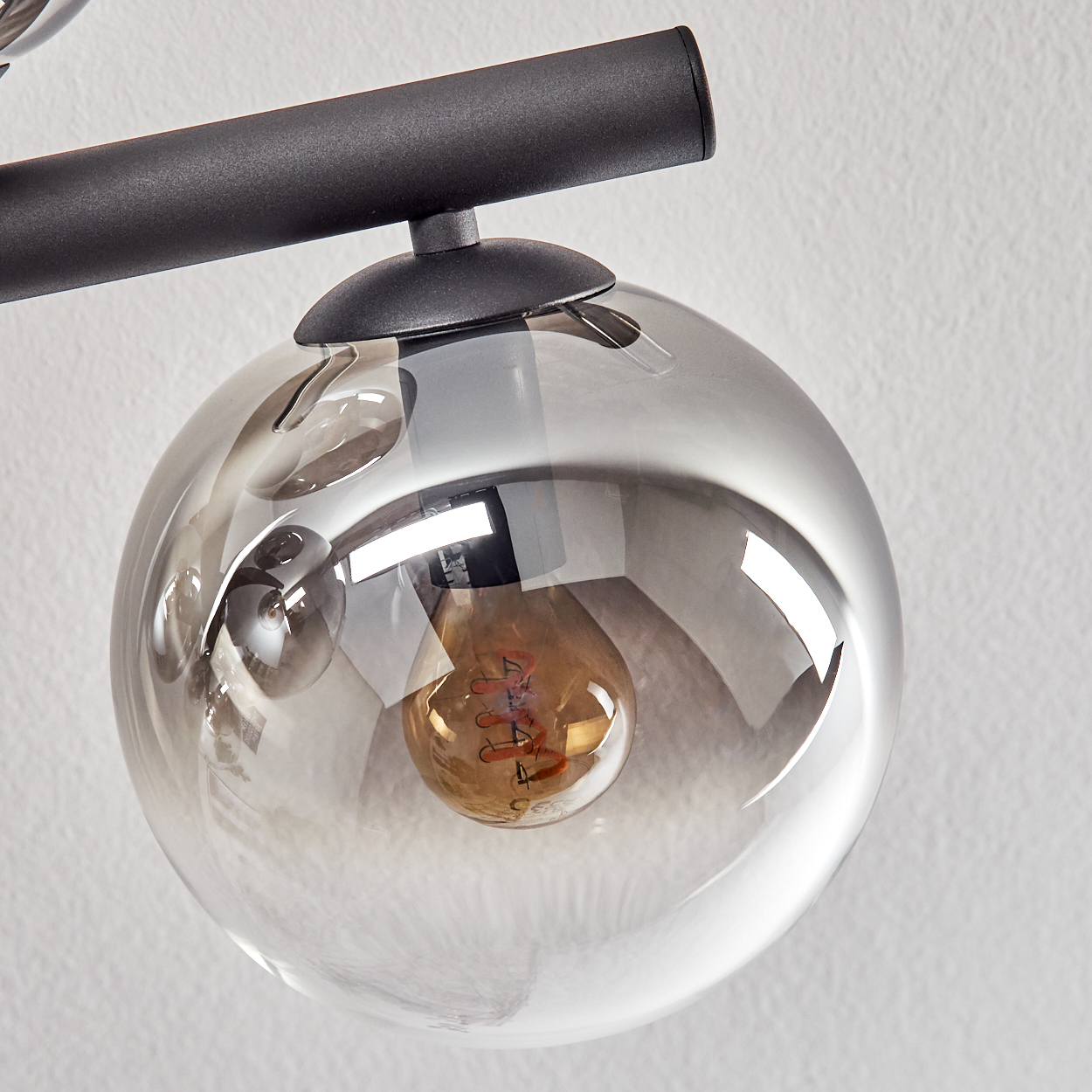 Nahaufnahme einer modernen Leuchte. Sie hat einen runden, klaren Glasschirm mit einer sichtbaren Glühbirne. Die Leuchte hat einen schwarzen Metallarm.