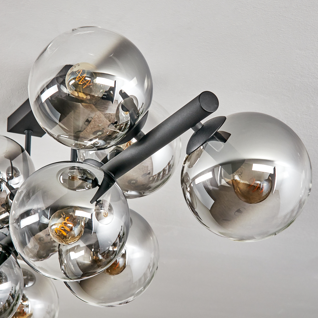 Nahaufnahme einer modernen Deckenleuchte mit mehreren kugelförmigen Glasschirmen. Jeder Schirm enthält eine Glühbirne, die an schwarzen Metallarmen aufgehängt ist.