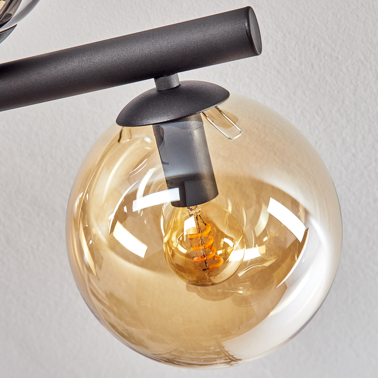 Nahaufnahme einer modernen Lampe mit schwarzem Rahmen und einer großen, bernsteinfarbenen Glaskugel mit Glühbirne.