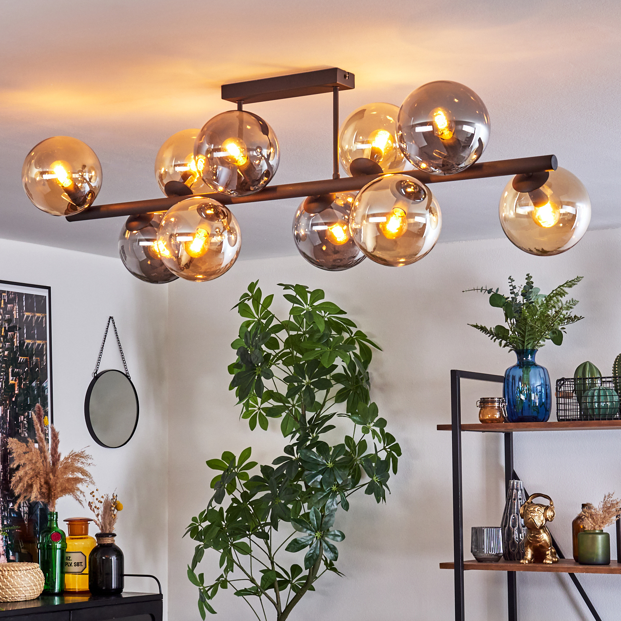 Ein modernes Wohnzimmer mit Kronleuchter, Pflanzen und Deko auf Regalen. Ein Spiegel hängt an der Wand.