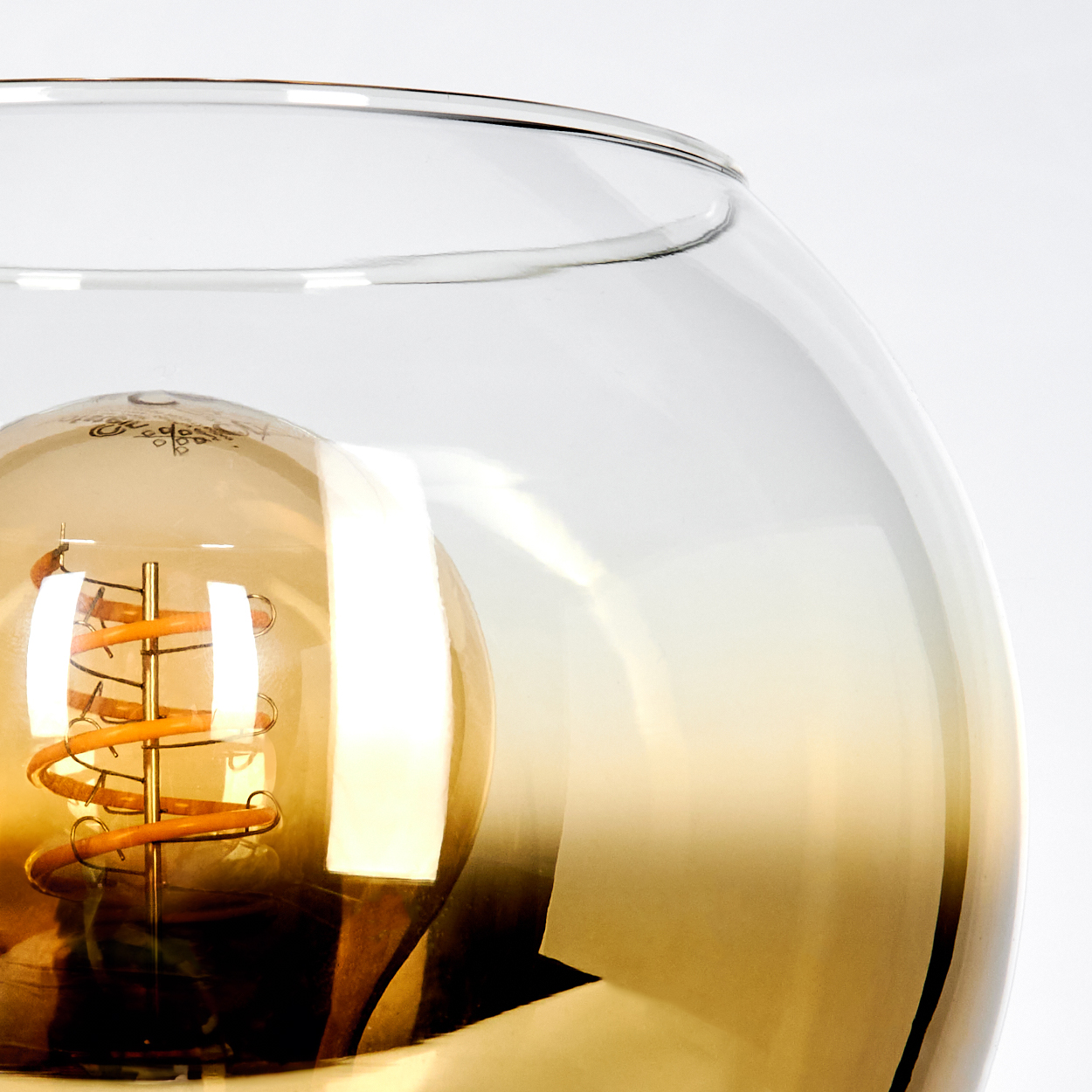 Nahaufnahme einer Glühbirne in einer Glaskugel. Der Glühfaden der Glühbirne ist spiralförmig. Das Glas hat einen Gelbverlauf.