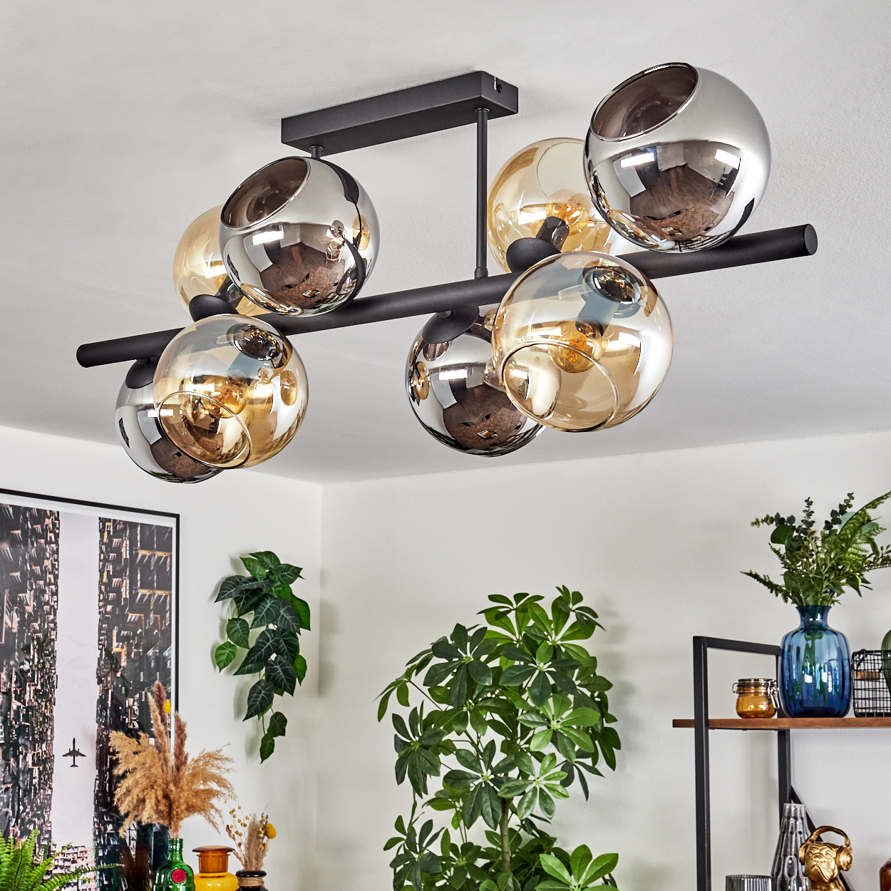 Eine moderne Deckenleuchte mit kugelförmigen Lichtern. Darunter sind Pflanzen und Dekorationen zu sehen. Das Licht hat schwarze Stangen und silberne und goldene Kugeln.