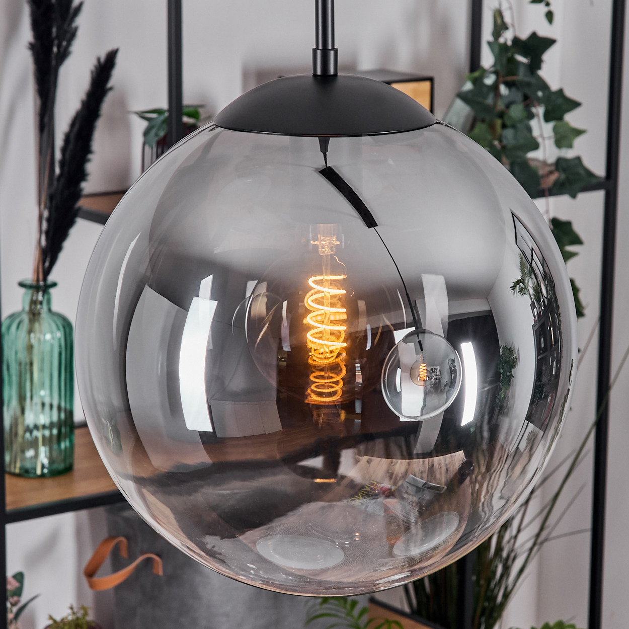 Moderne, rauchfarbene Glaskugel-Pendelleuchte mit warmer Spiralbirne. Der Hintergrund zeigt Regale mit Dekoration.