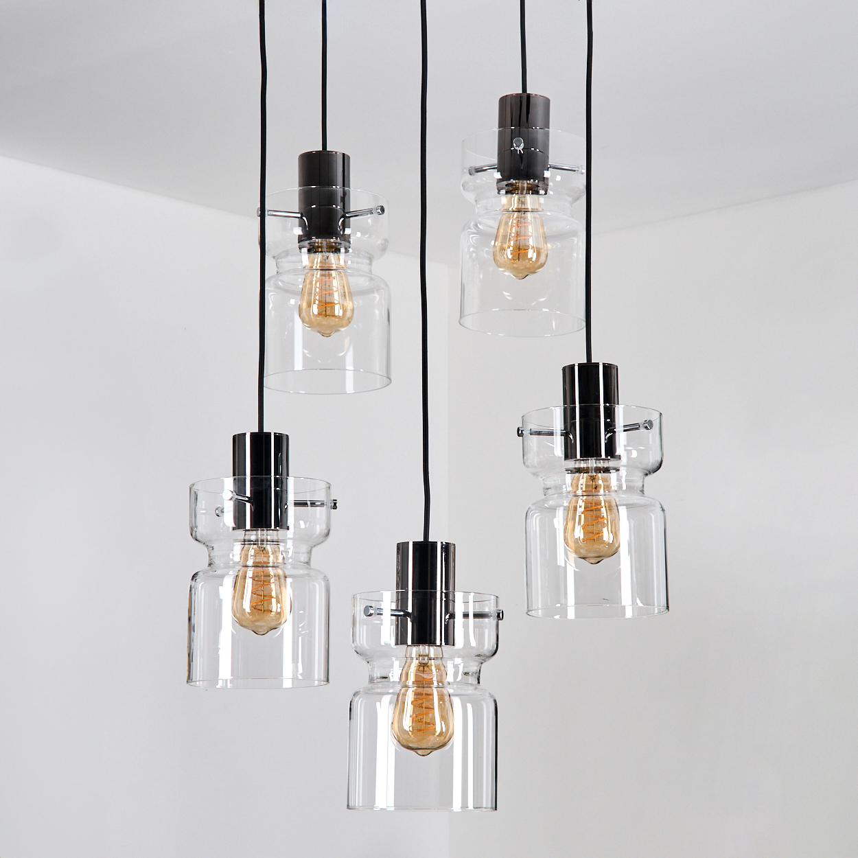 Fünf gläserne Pendelleuchten mit Edison-Glühbirnen hängen an schwarzen Kabeln vor weißem Hintergrund.