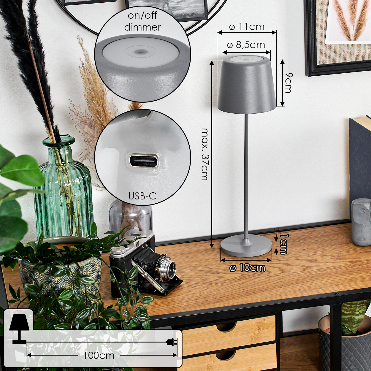 Eine graue Schreibtischlampe mit Maßen, eine Kamera und Pflanzen stehen auf einem Holztisch. Details umfassen USB-C und einen Ein/Aus-Dimmer.