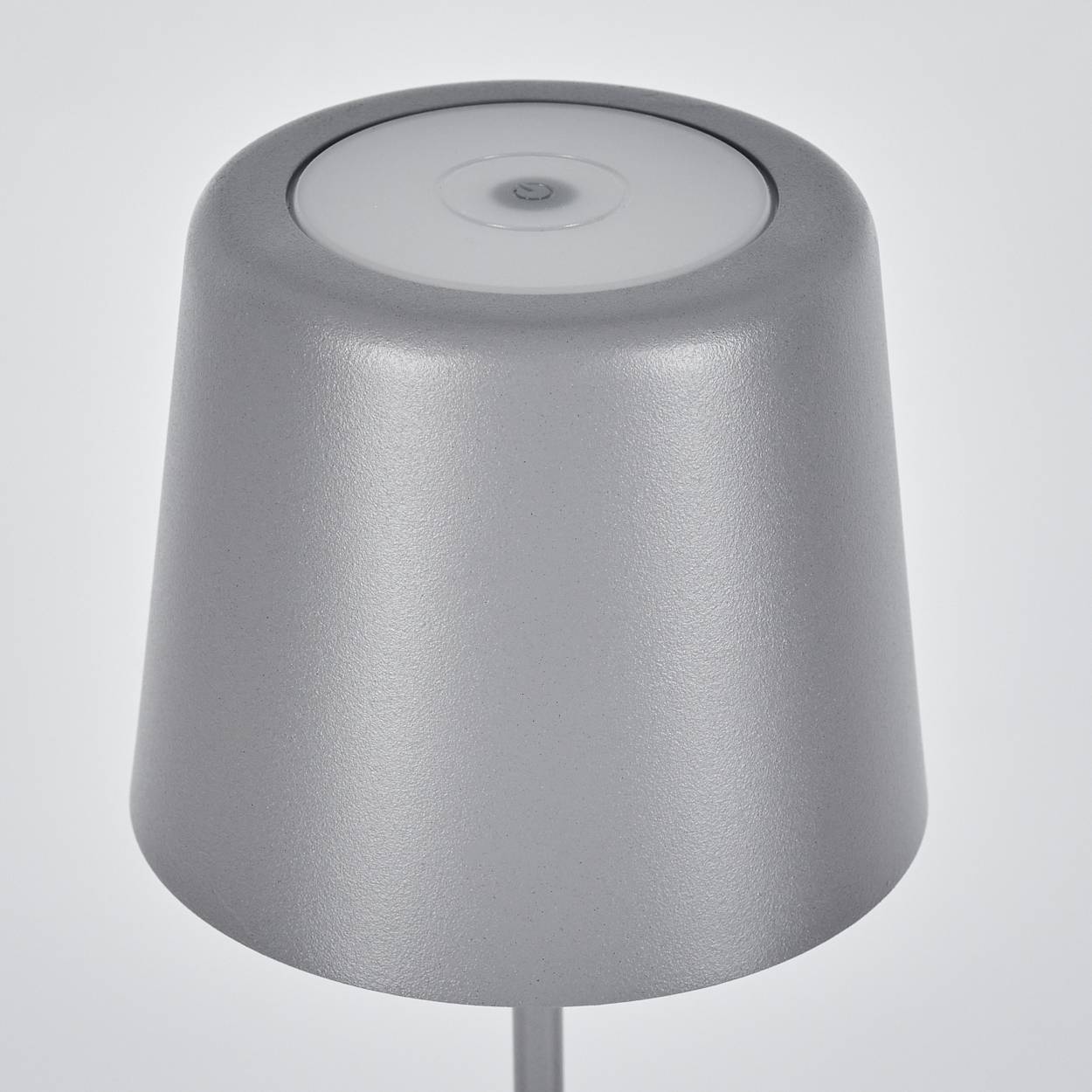 Eine graue, moderne Lampe mit rundem, konischem Schirm und hellem, kreisförmigem Licht oben. Der Hintergrund ist weiß.