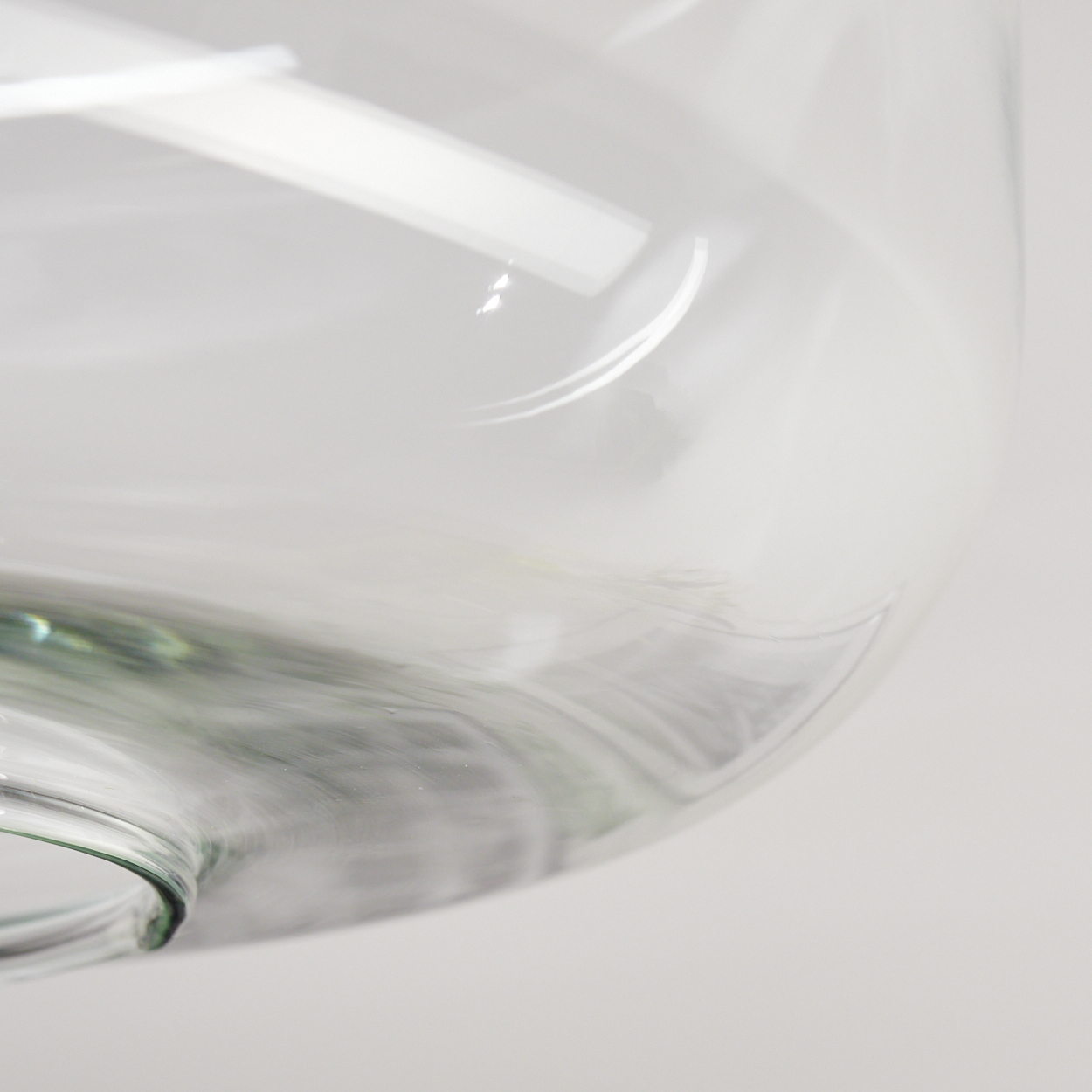 Nahaufnahme eines transparenten Glasobjekts. Das Glas hat eine gebogene Form, mit abgerundeter Oberseite und leichtem Grünstich.